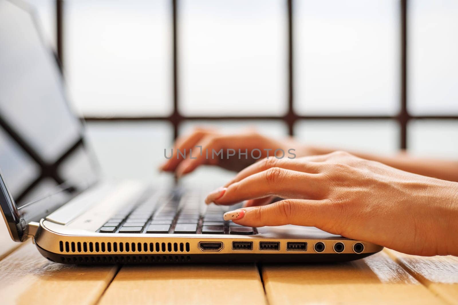 A woman working on laptop at wooden table, hands close up. Woman working on laptop in a cafe.