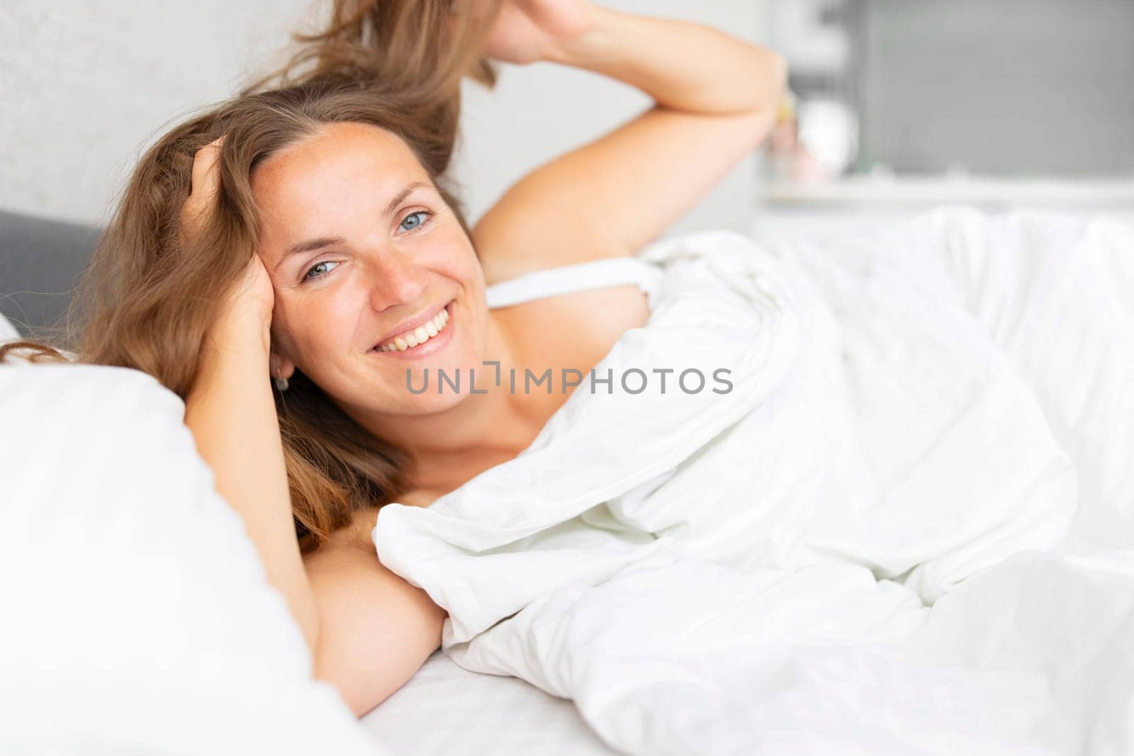 Young smiling attractive brunette woman lies in a big white bed.