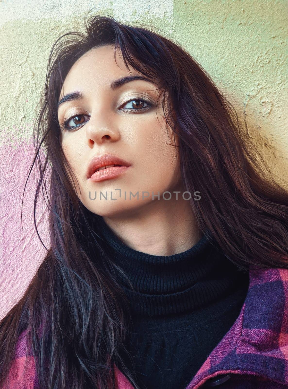 Half-profile portrait of a charming woman with dark hair in black golf against the background of a colored wall.