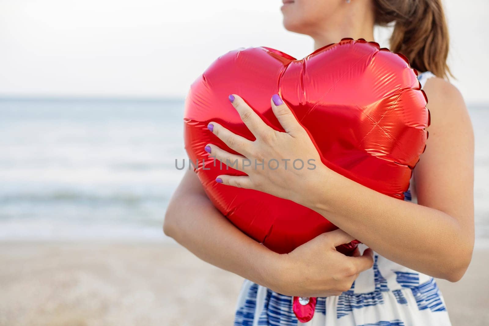 Happy young woman huging heart-shaped balloon on the beach.