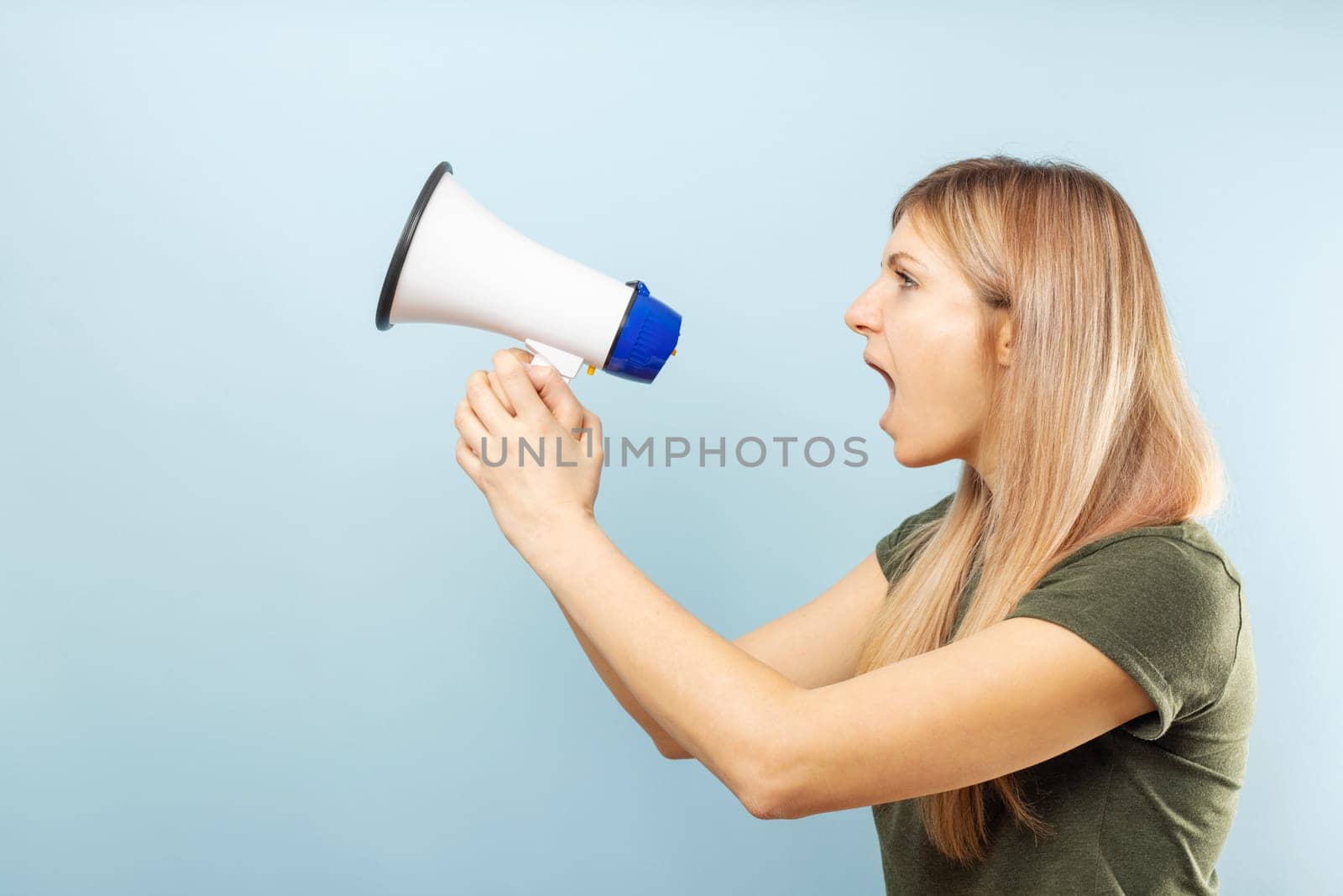 Young blonde woman shouting loudly while holding a megaphone on blue background. Concept of speech and announce, idea for marketing or sales.