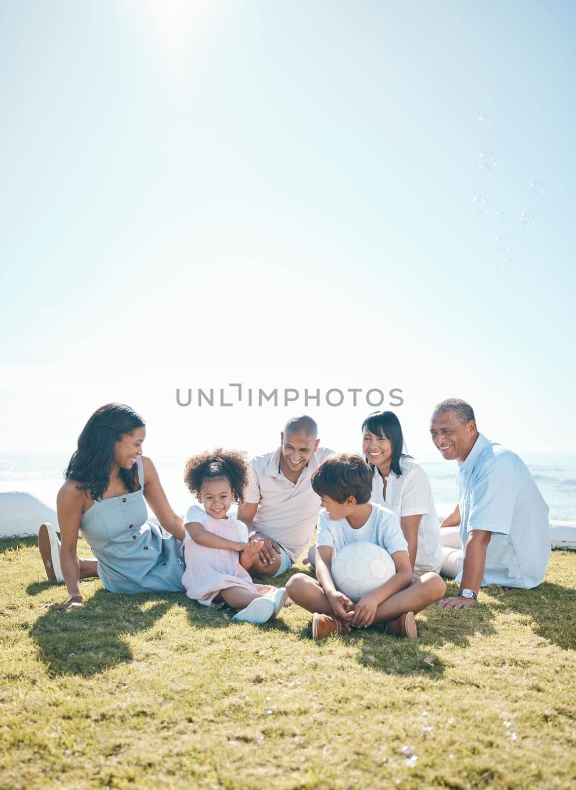 Parent, children and generations are relaxing on grass in summer for quality time on holiday in mockup space. Happiness, kid and big family in outdoor for bond at resort with ball at house or ocean. by YuriArcurs