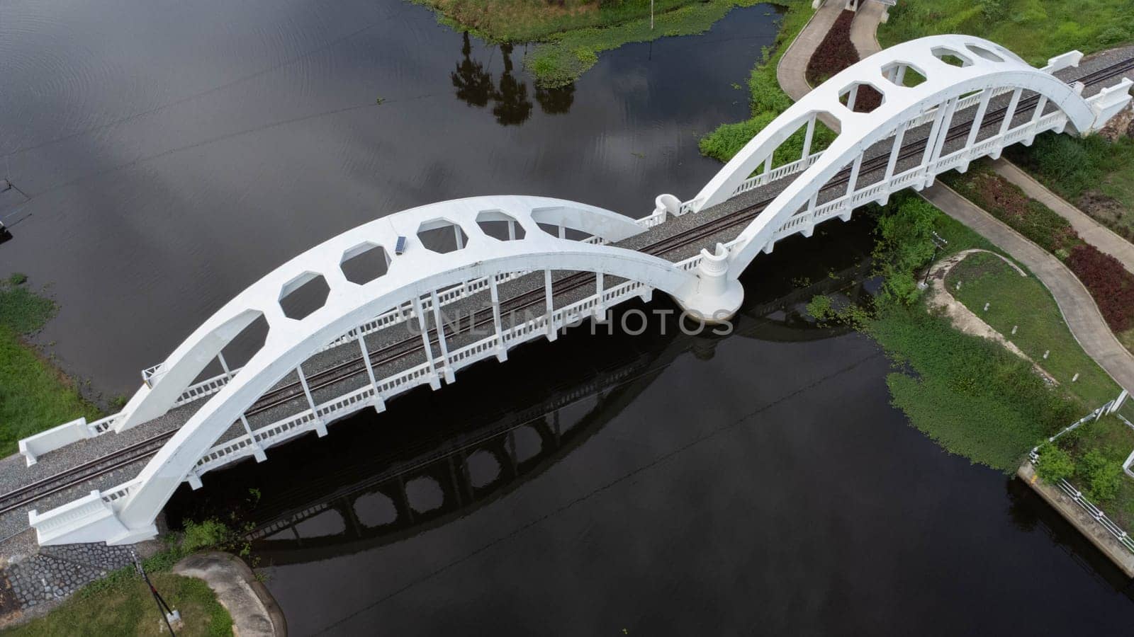 Aerial view of Tha Chomphu White Bridge, Lamphun, Thailand. Old railway bridge over river with nature background, forest and green mountains. Tourist attraction landmark. by TEERASAK