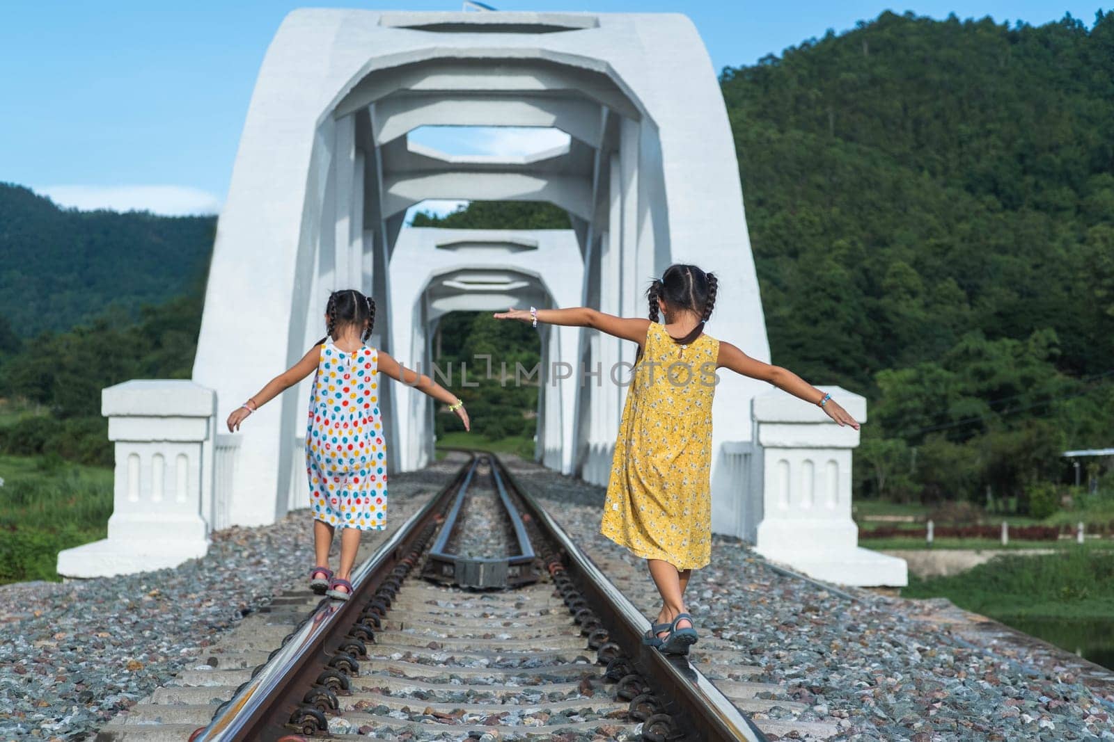 Children playing outside on train tracks. Asian sisters walking on the railway in rural scene.