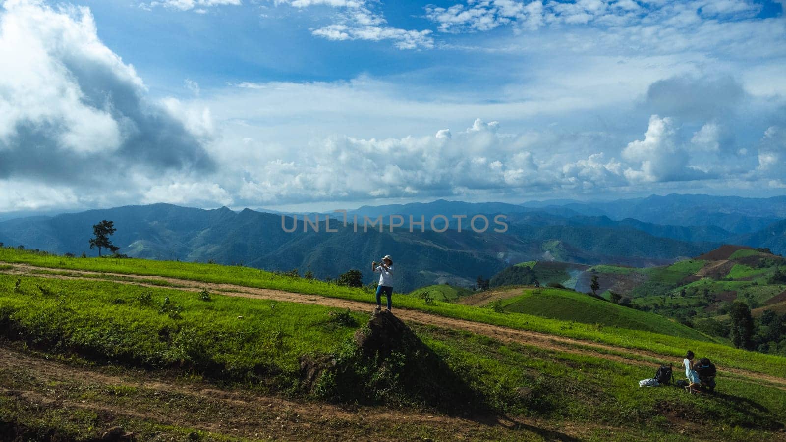 Tourists stand on the rocks enjoying the picturesque hillside views with vast fields on a beautiful sunny day with blue sky and clouds in springtime. by TEERASAK