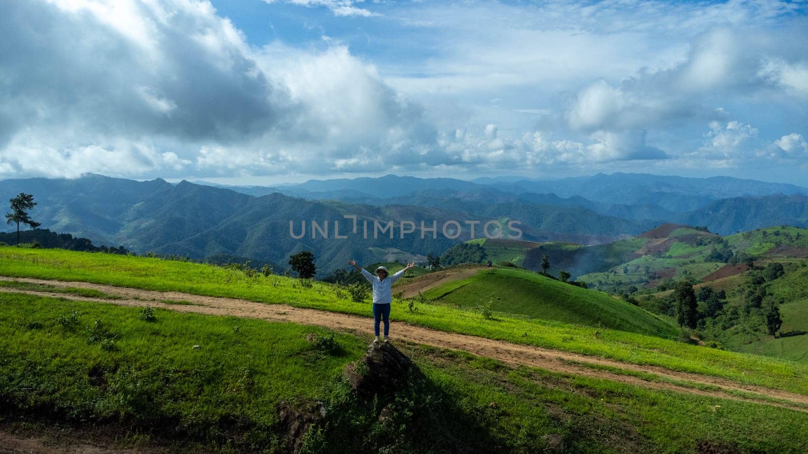 Tourists stand on the rocks enjoying the picturesque hillside views with vast fields on a beautiful sunny day with blue sky and clouds in springtime.