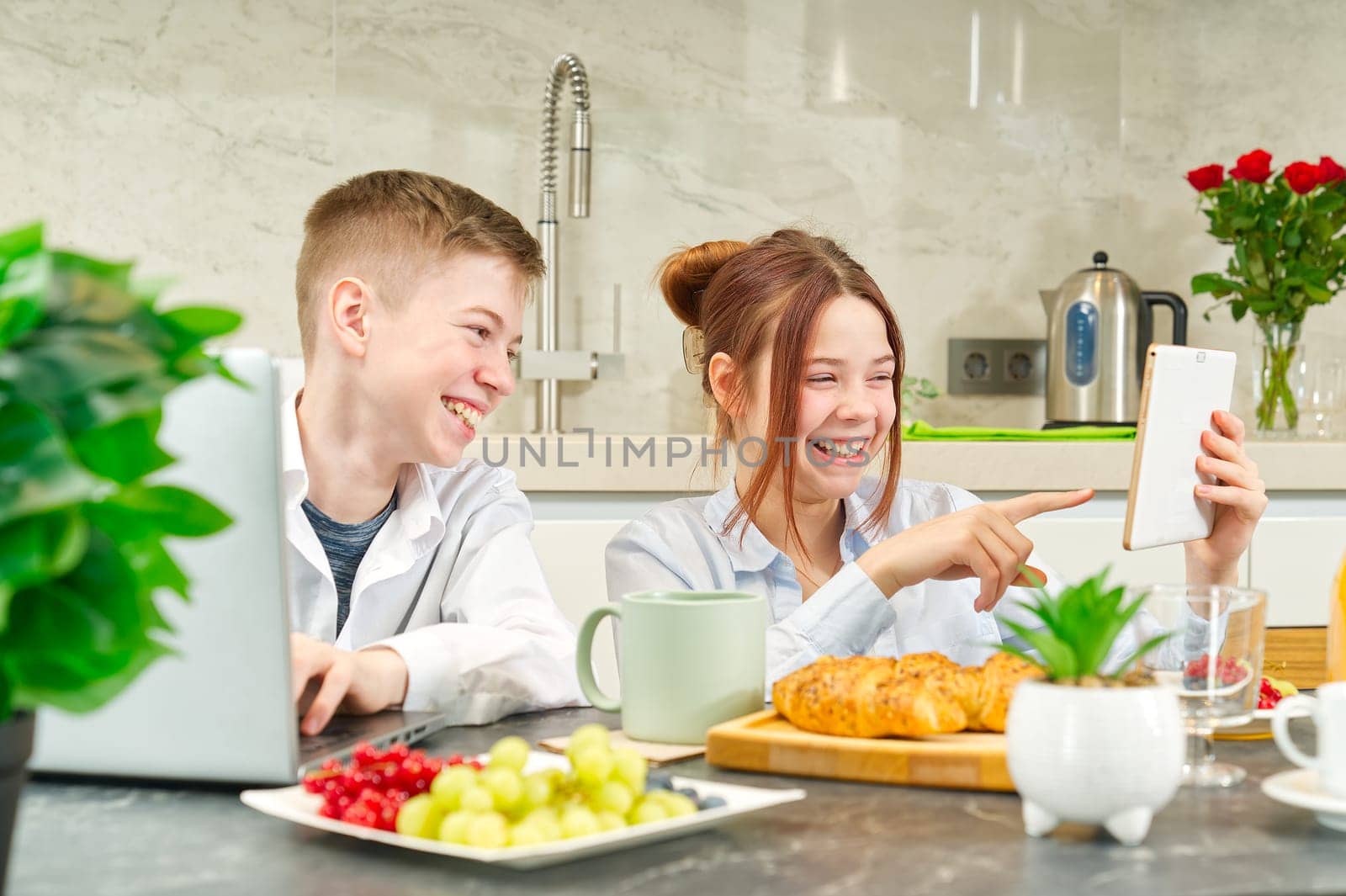 Happy childrens, kids having healthy breakfast at home and using digital devices. kids playing and eating. Using notebook in kitchen at breakfast time