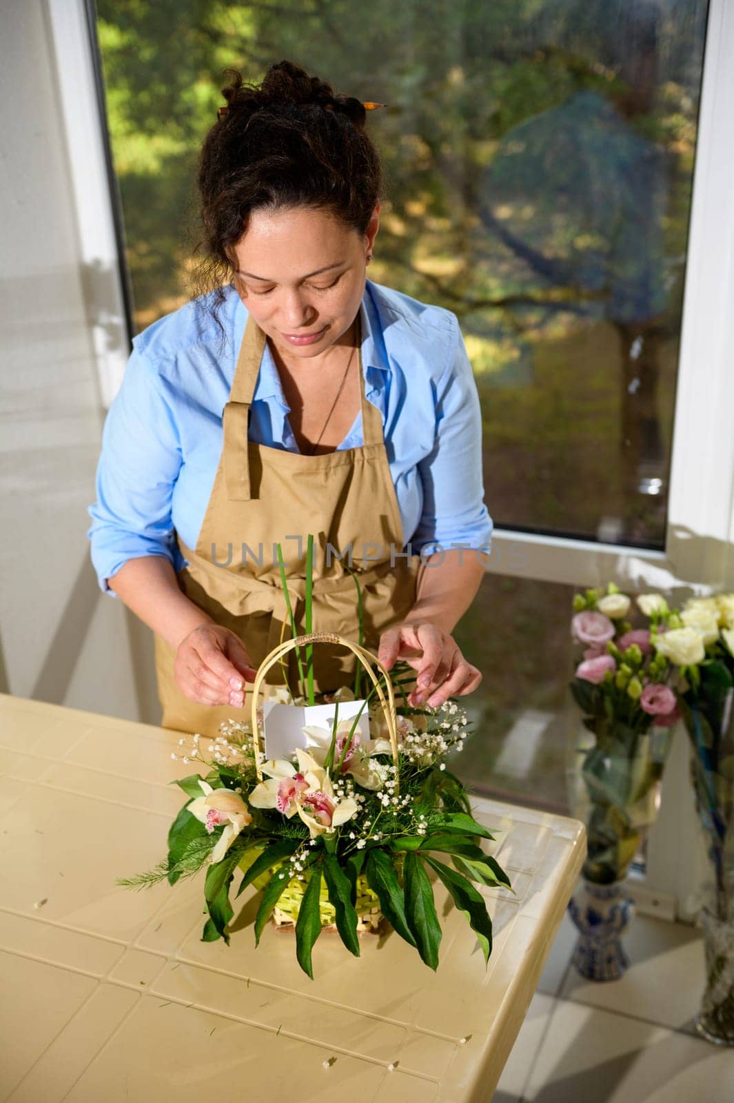 Florist creating a flower arrangement with fresh orchid flowers and plants, inserting a birthday card, in floral shop by artgf