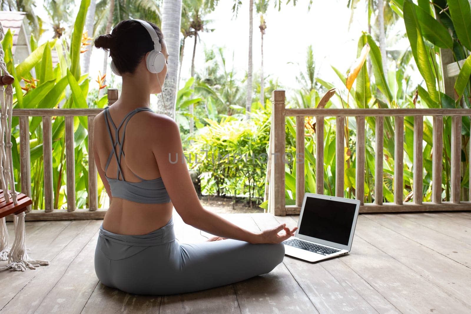 Young woman in sports clothing following online meditation using laptop and headphones outdoors. Spirituality and mental health concept.