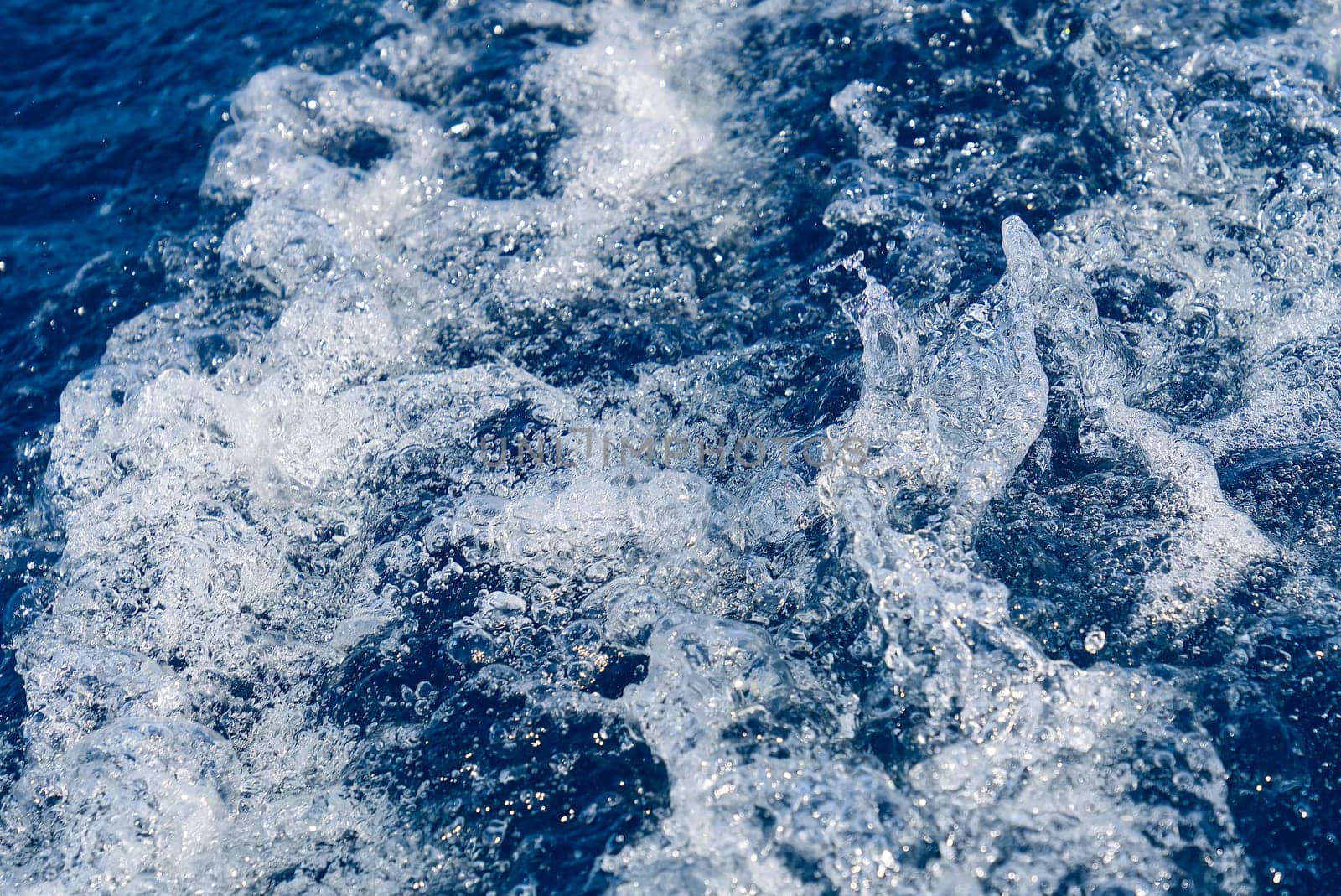 Abstract blue sea water with white waves. Blue sea texture with waves and foam. Rough deep turquoise and blue Mediterranean sea. Sea water top view.