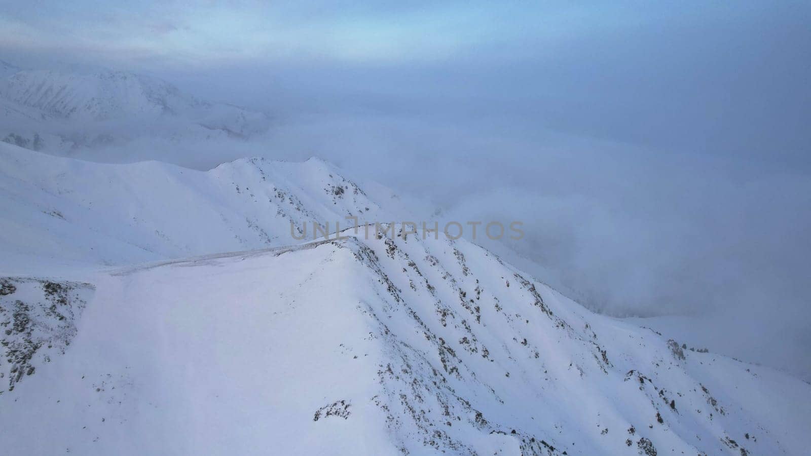 Mystical dawn with clouds in snowy mountains. The white hills are covered with clouds and snow. Steep rocky cliffs. The high peaks of the peaks. The rays of the sun at dawn pass through the clouds