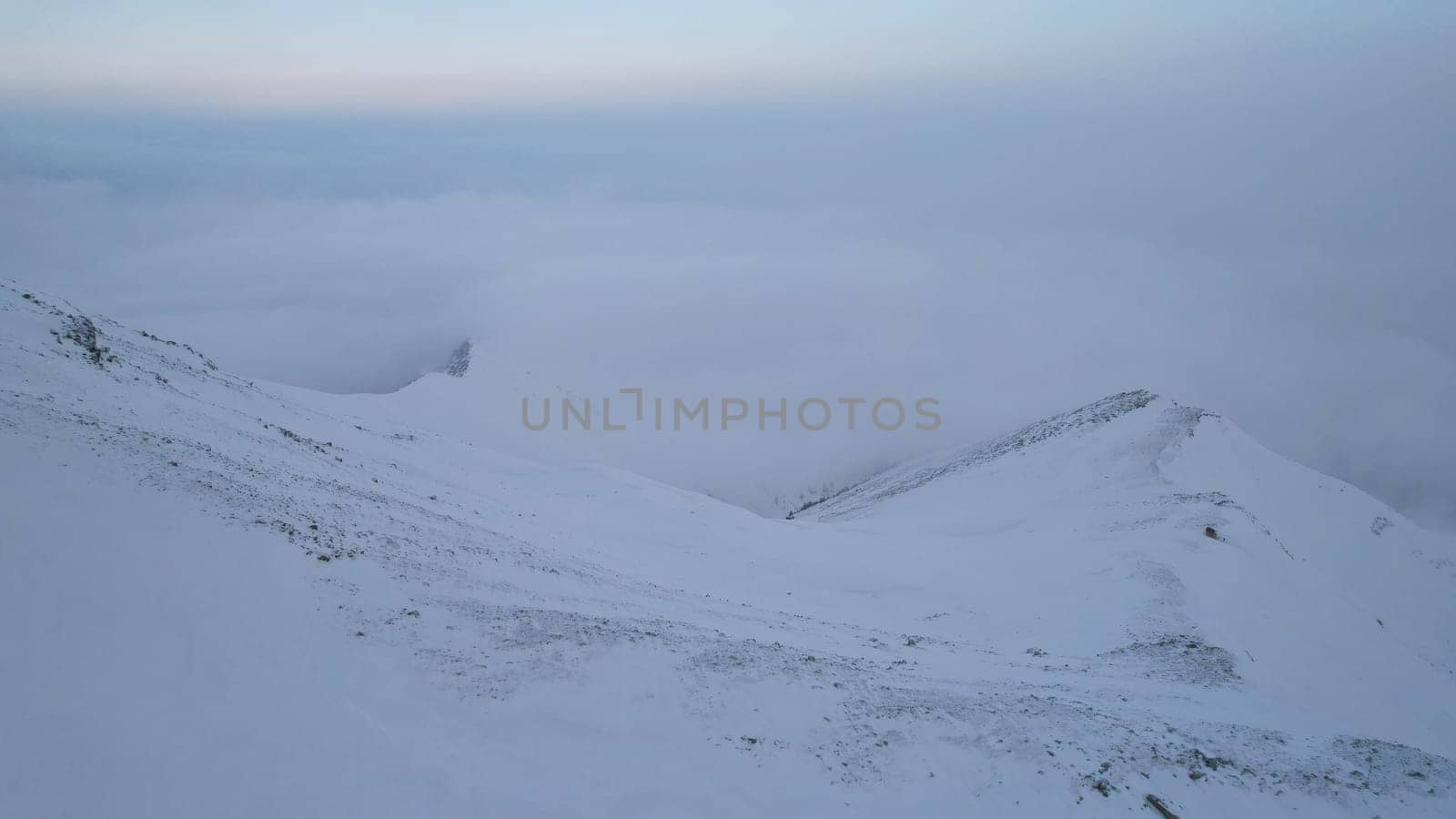 Mystical dawn with clouds in snowy mountains. The white hills are covered with clouds and snow. Steep rocky cliffs. The high peaks of the peaks. The rays of the sun at dawn pass through the clouds