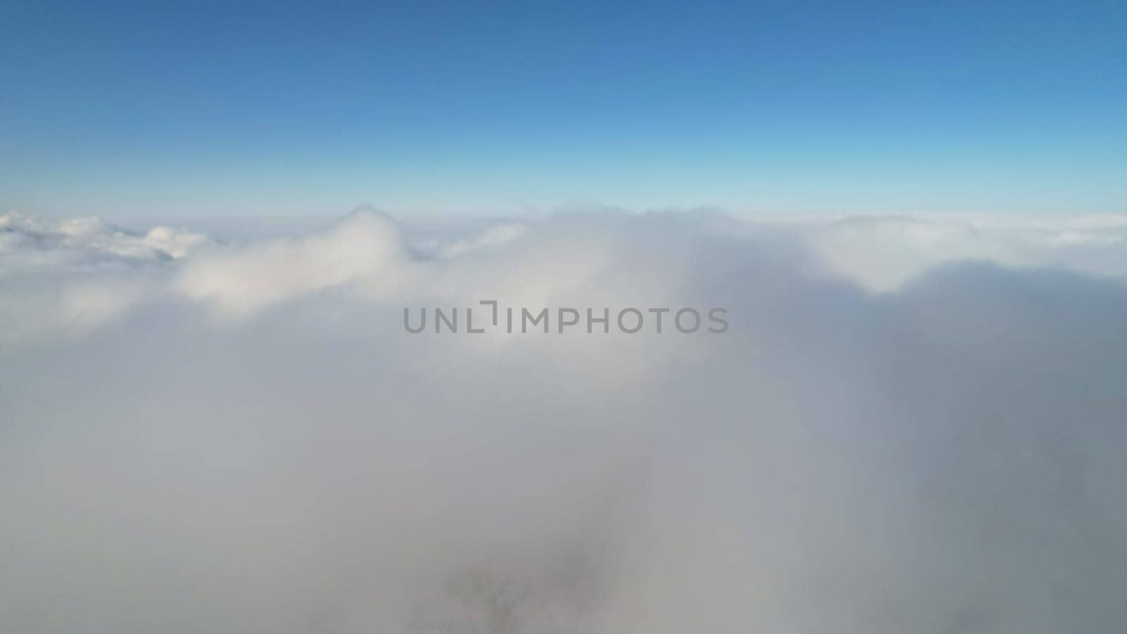 White cumulus clouds in snowy mountains in winter. The rays of the sun fall on part of the clouds, a shadow comes from the peak. Blue clear sky. Christmas trees grow on the hills. Tourists are walking