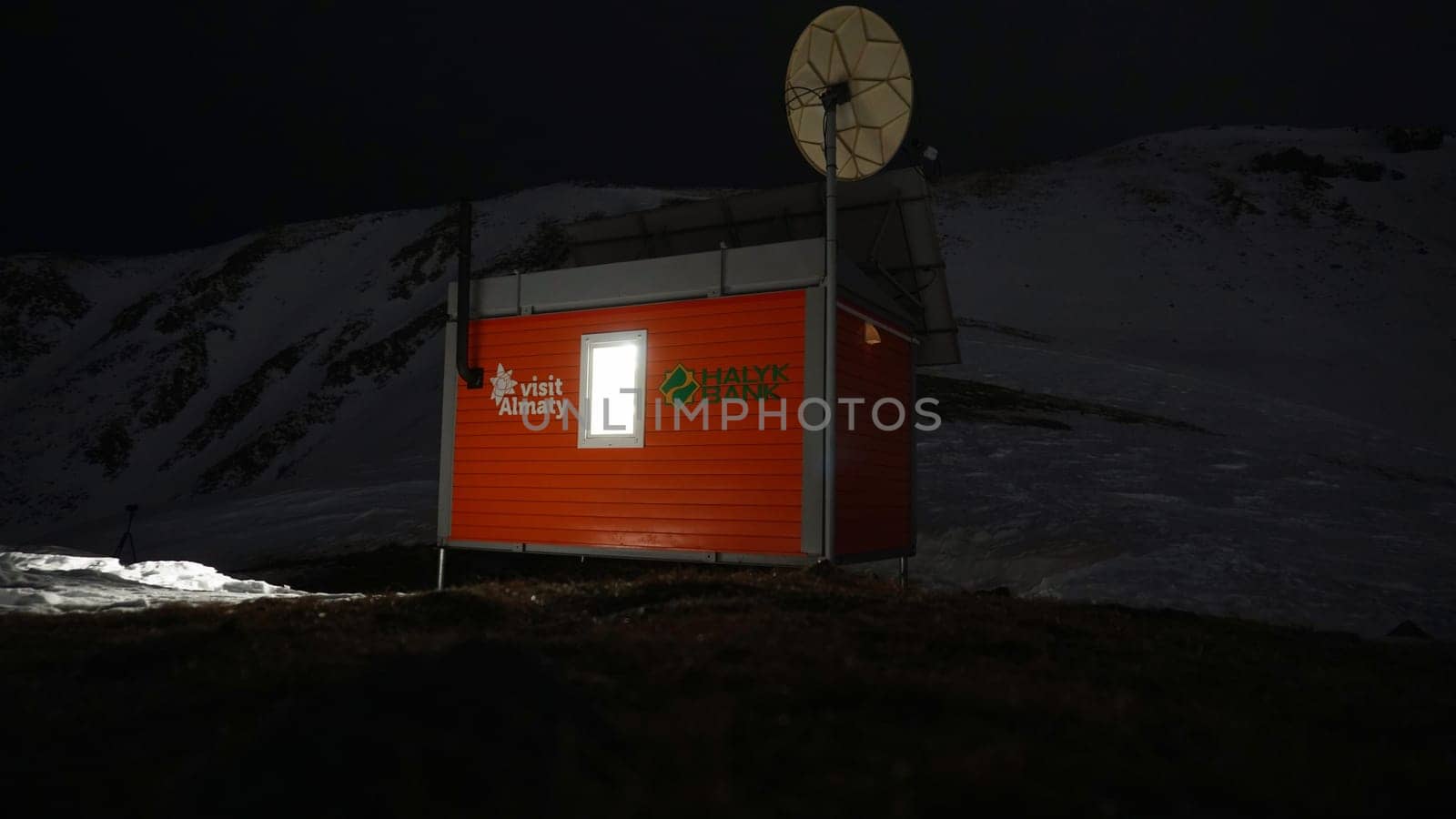 Modern rescue hut in the mountains at night. The van is equipped with rescue equipment. Installed satellite dish, oven, chimney, light, insulated. Winter, lots of snow. A house high in the mountains