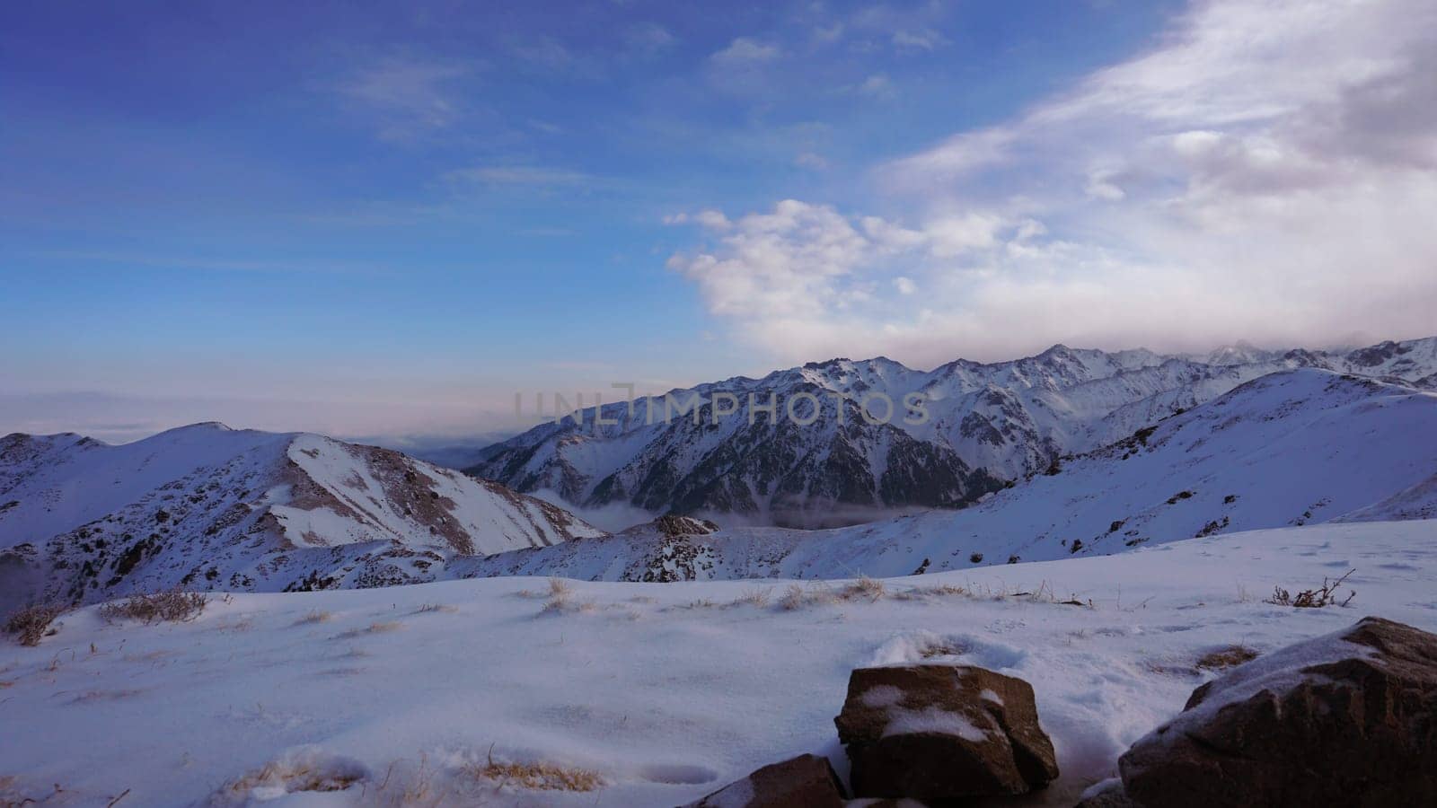 An ocean of clouds in the snowy mountains at dawn. White clouds are like a carpet in a gorge. Waves rise and descend from the mountains. Sunrise of the yellow sun. There are stones lying. Kazakhstan