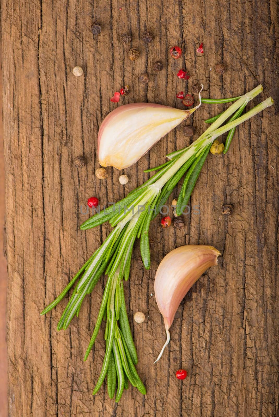 wooden culinary background with garlic, rosemary, bay leaves, pepper and some cloves pictured on it by aprilphoto