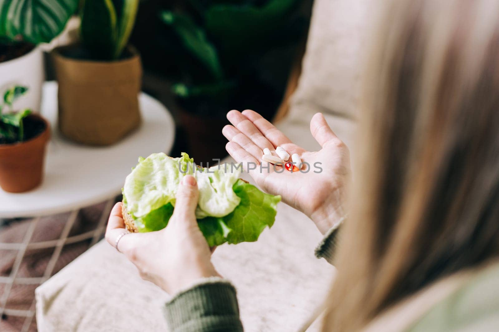 Close up of woman hands holding and choosing vegetables or tablet vitamin pills. Girl in living room with plants at home, healthy lifestyle concept.