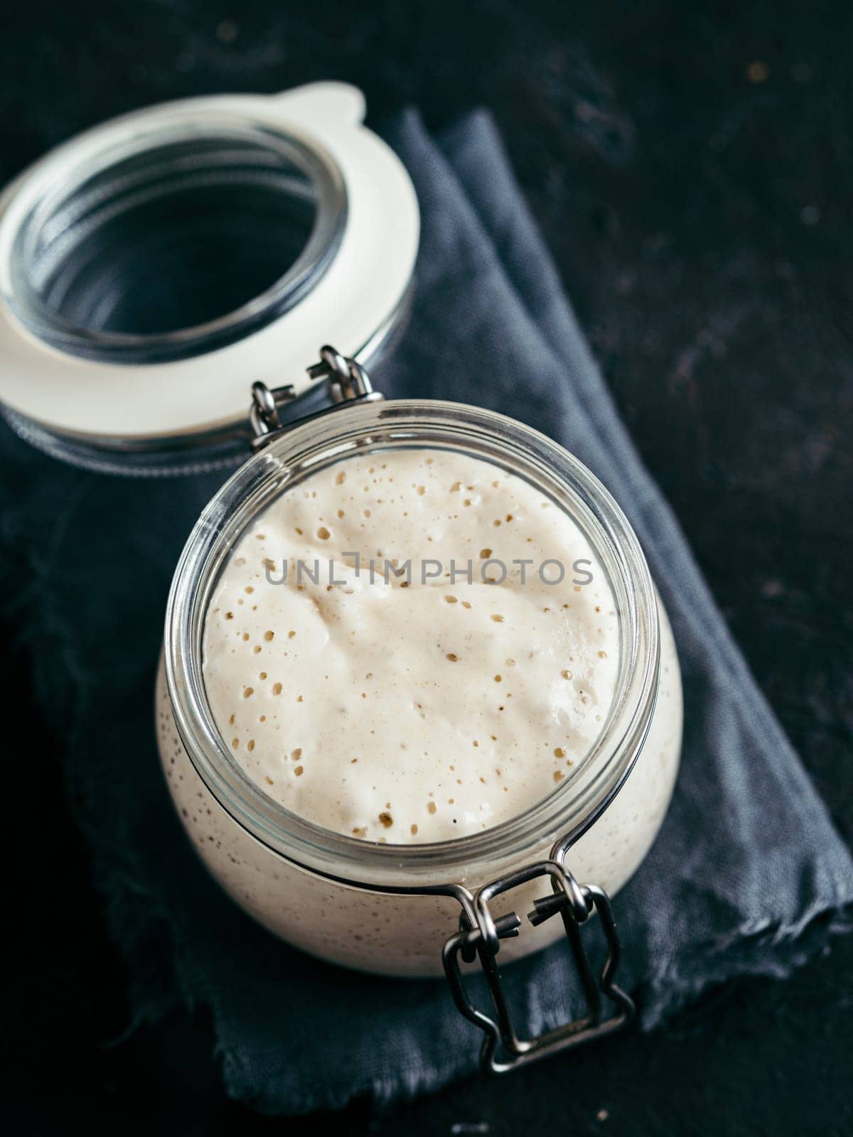 Wheat sourdough starter. Glass jar with sourdough starter on dark background, copy space. Vertical.