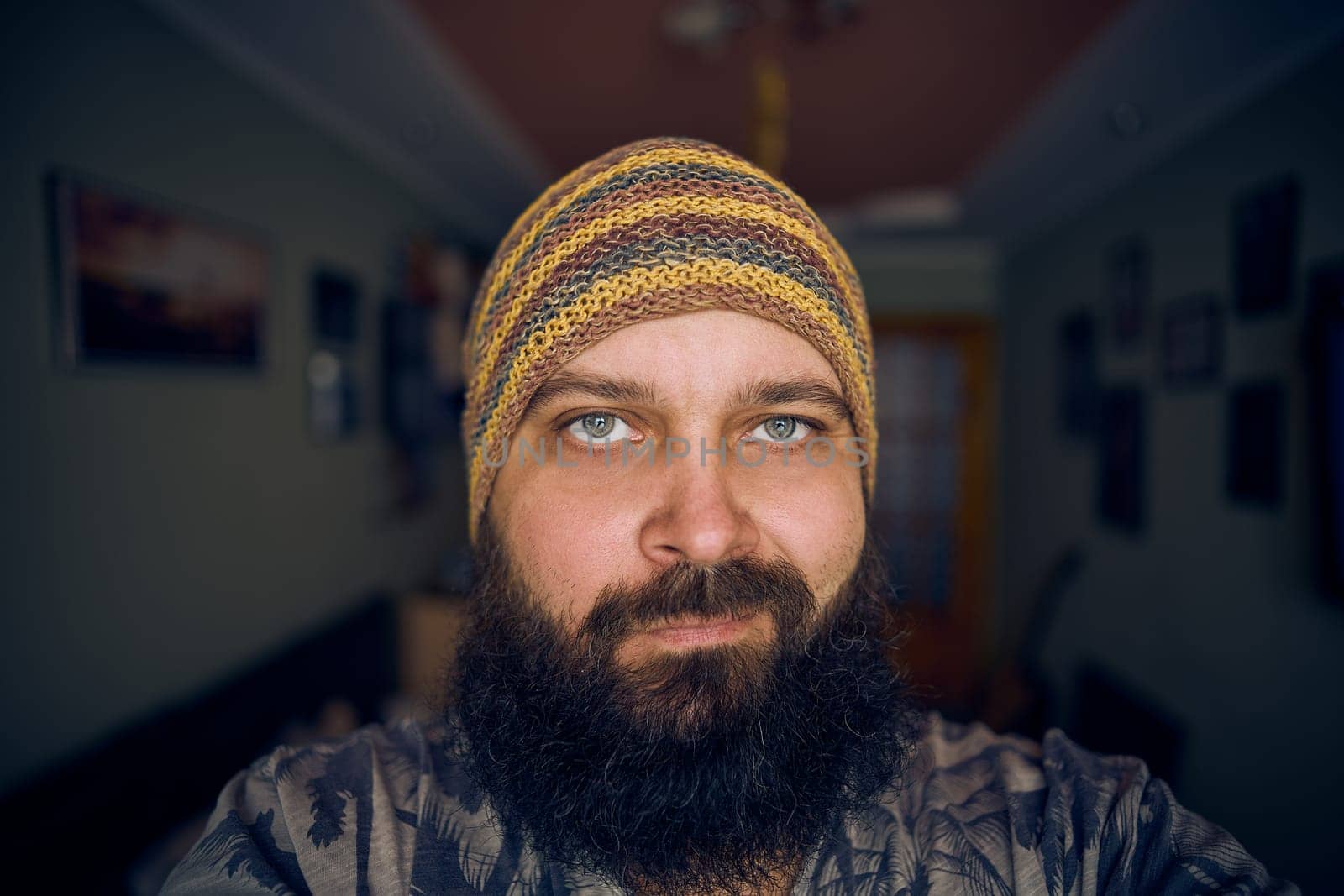 A man with a beard wearing a striped hat and shirt, looking up into the camera
