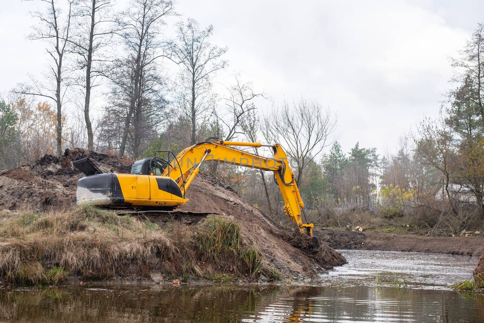 Yellow excavator shoveling dirt from the bottom of an artificial pond