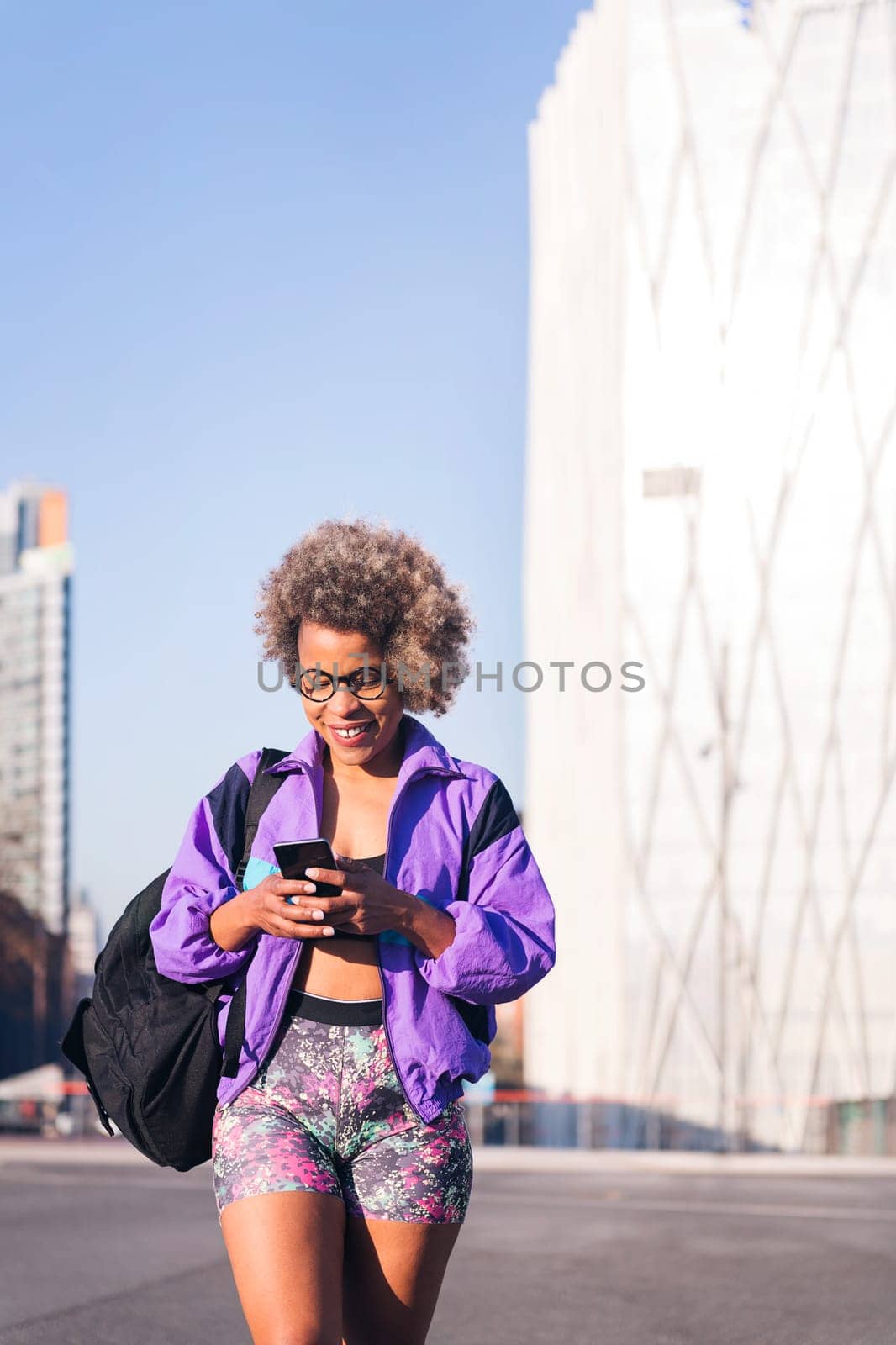 vertical portrait of a woman in sports clothes using a mobile in the city, concept of technology of communication and urban sport