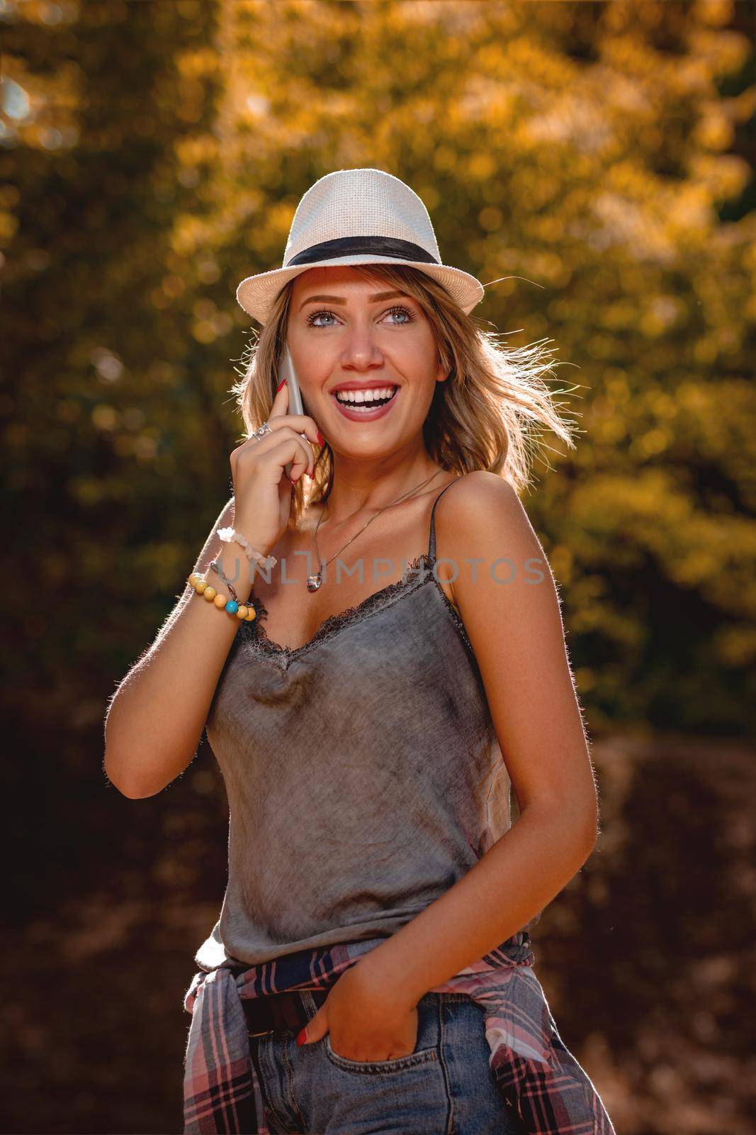 Beautiful smiling young woman with summer hat enjoying in the nature in autumn and talking on smartphone.
