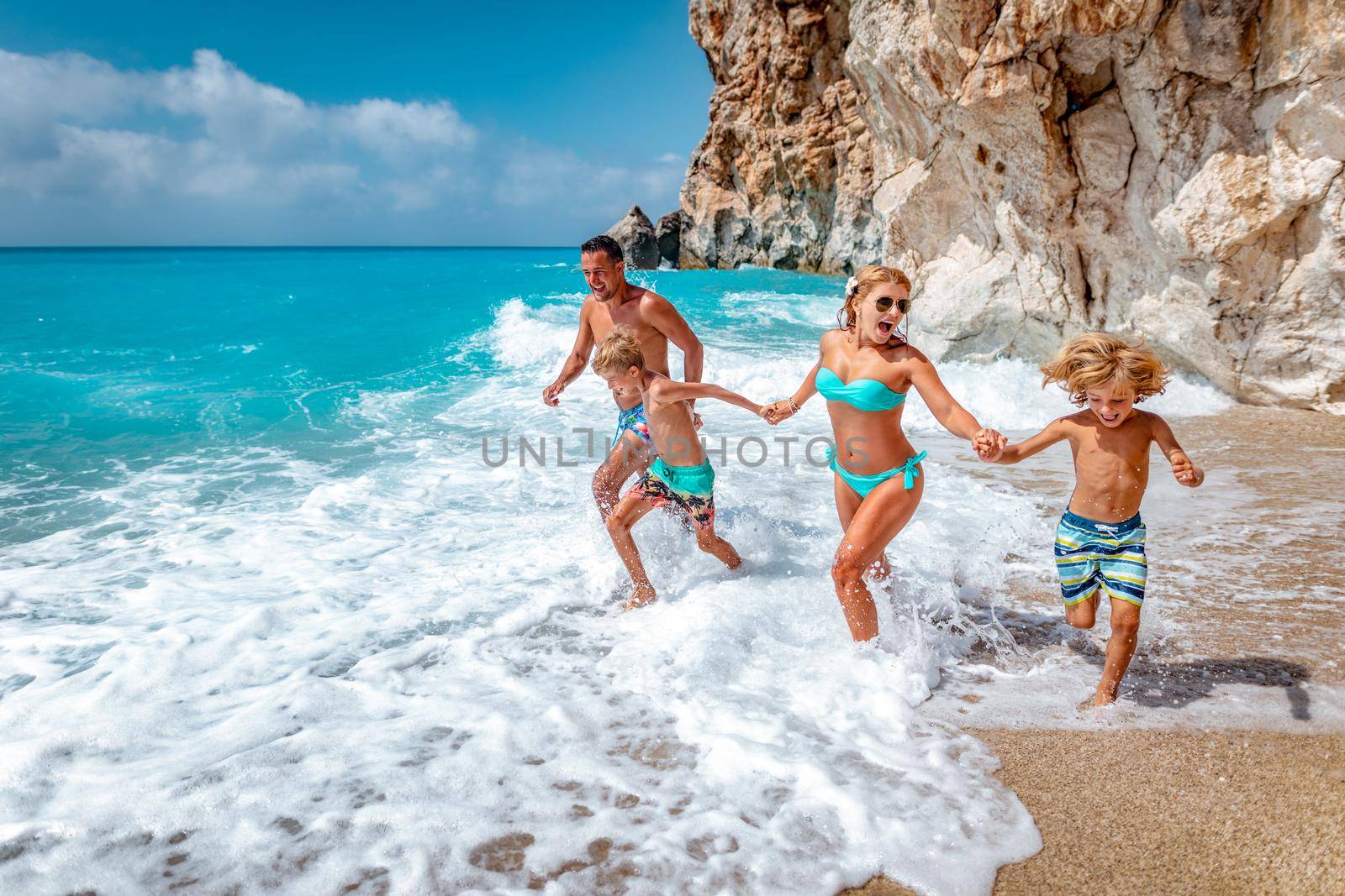 Mother father and children are running on summer beach. 