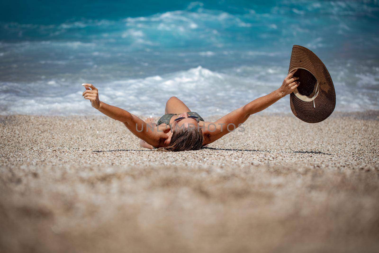 A young woman relaxing on the beach. She is lounging and sunbathing on the coast in the sea.