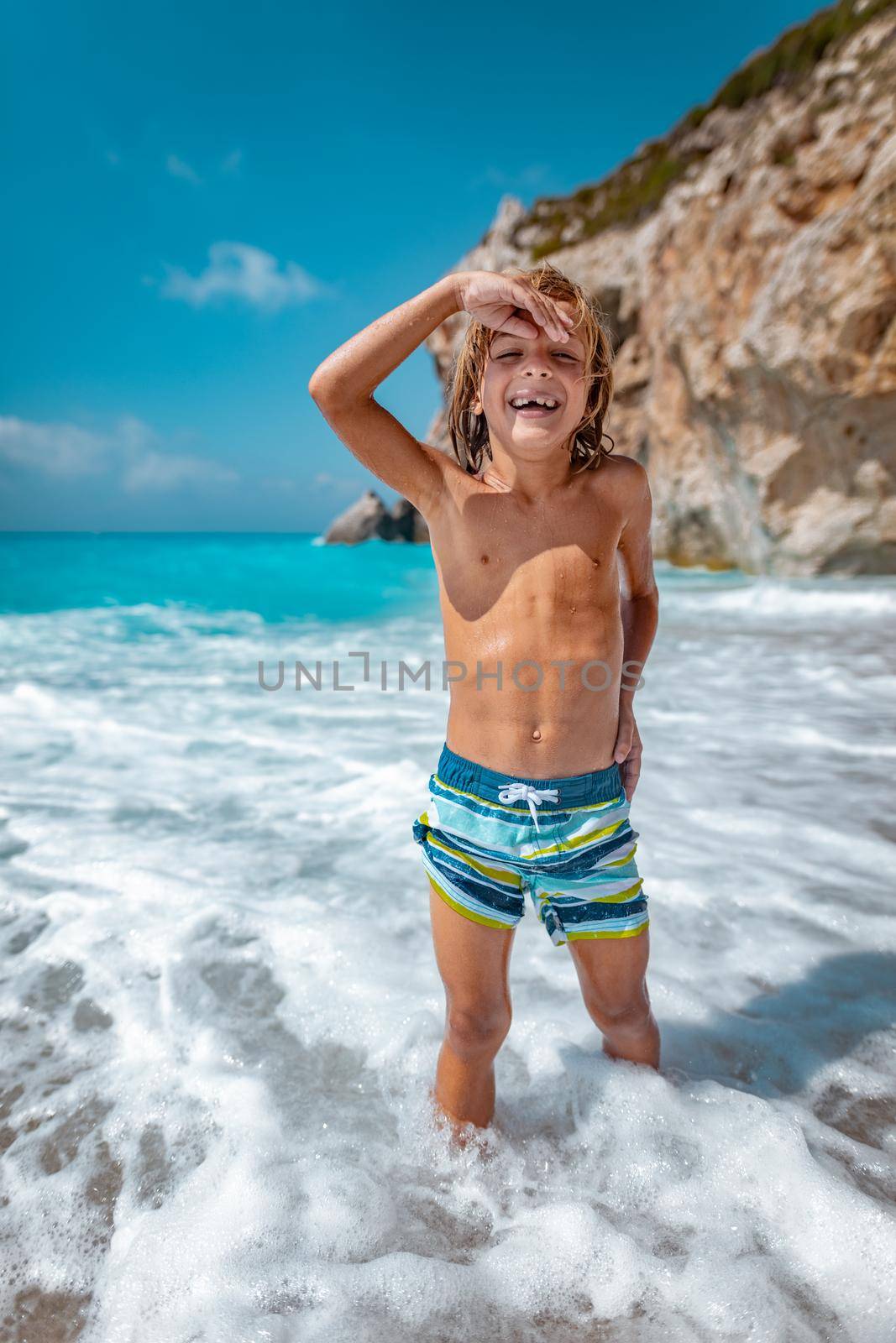 Cute boy enjoying on the beach standing in the sea waves. 
