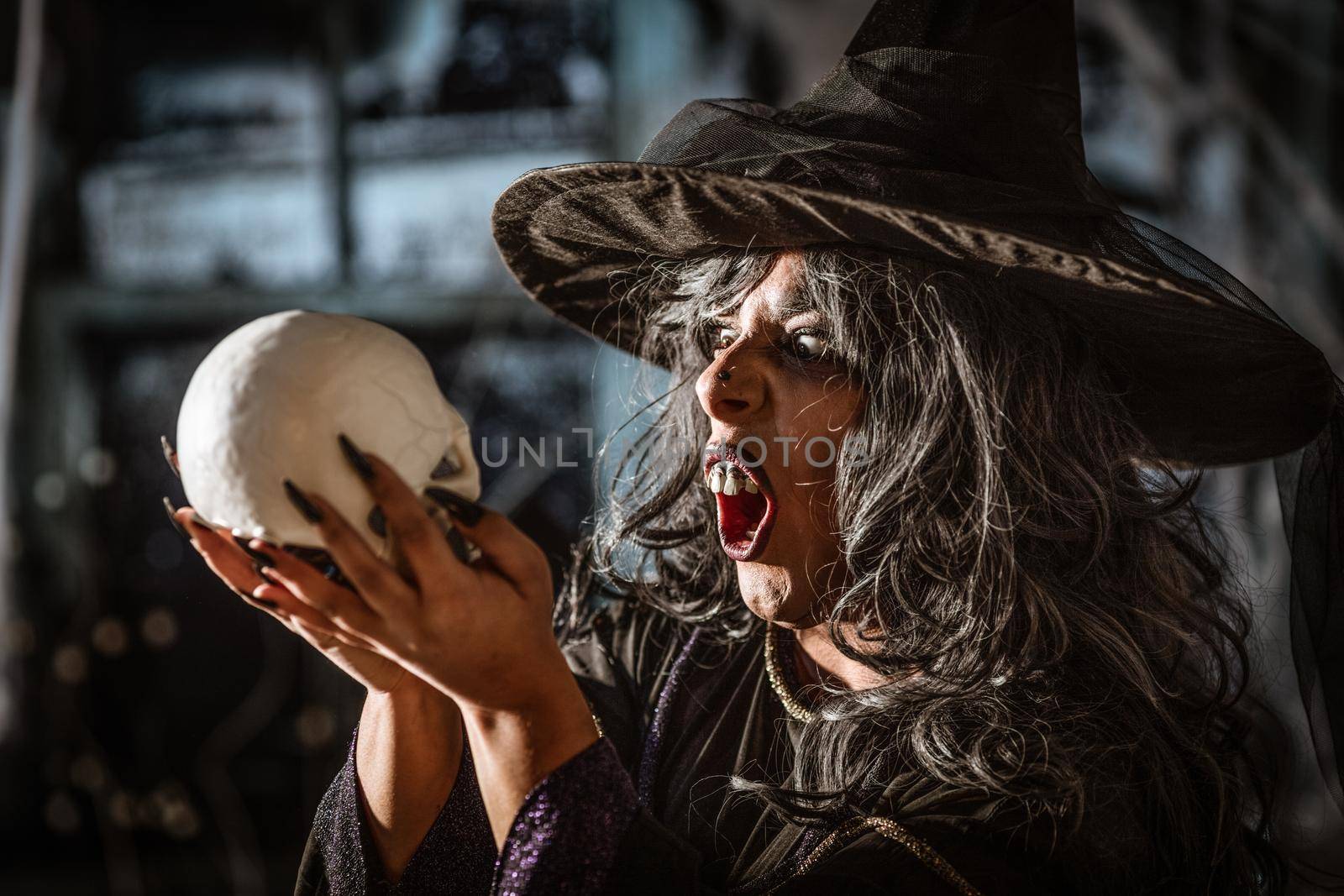 Portrait of witch with awfully face in creepy surroundings and smoky green background talks with dead. Halloween concept.