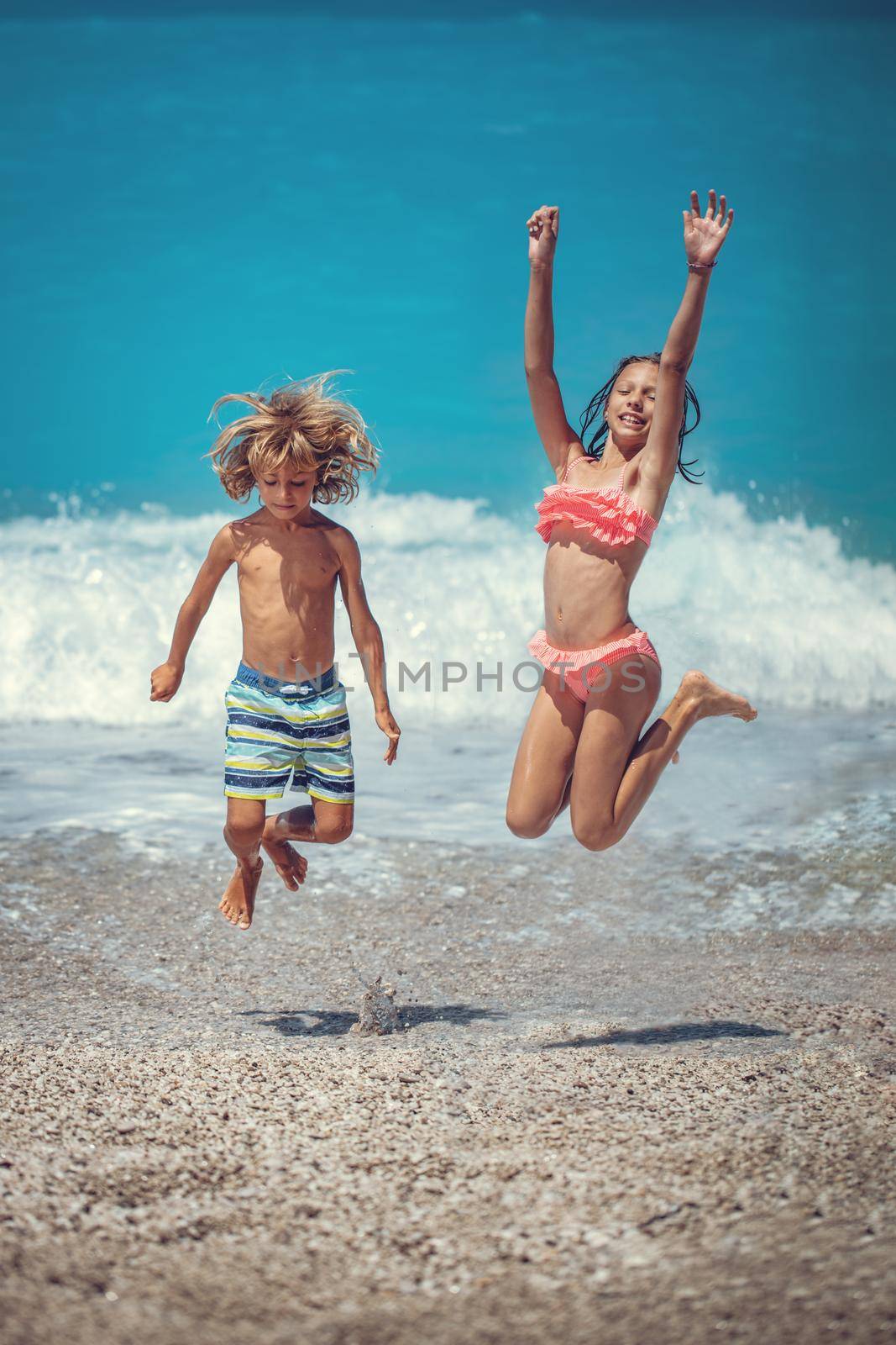 Brother and sister are playing and having fun in the shore on the beach during the hot summer vacation day. They are enjoying and jumping on the beach.