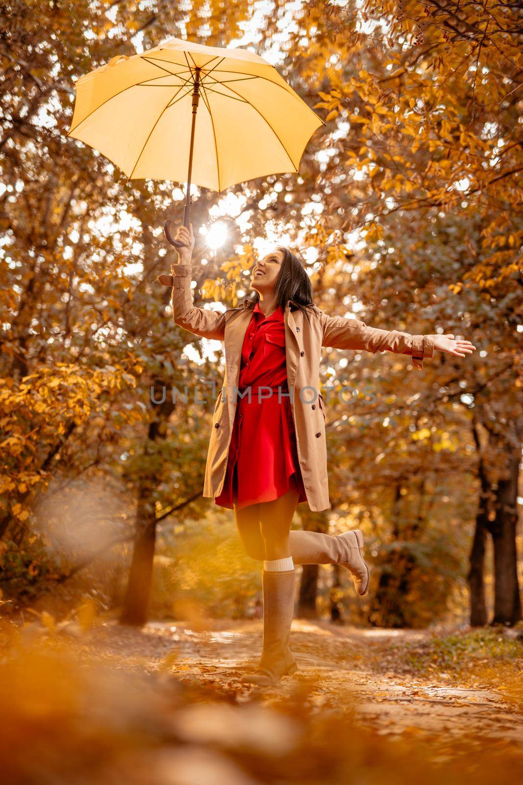 Happy young woman walking in autumn sunny park, holding umbrella height above her head.