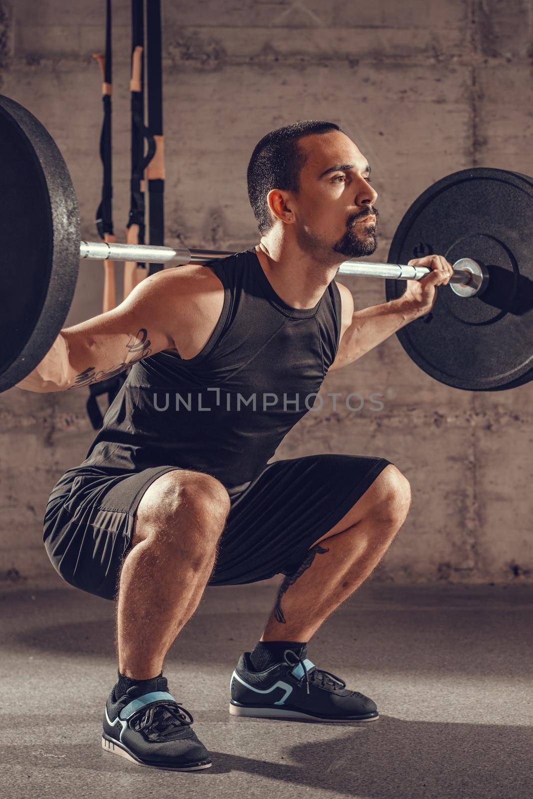 Handsome young muscular man doing squat exercise with barbell at the gym.