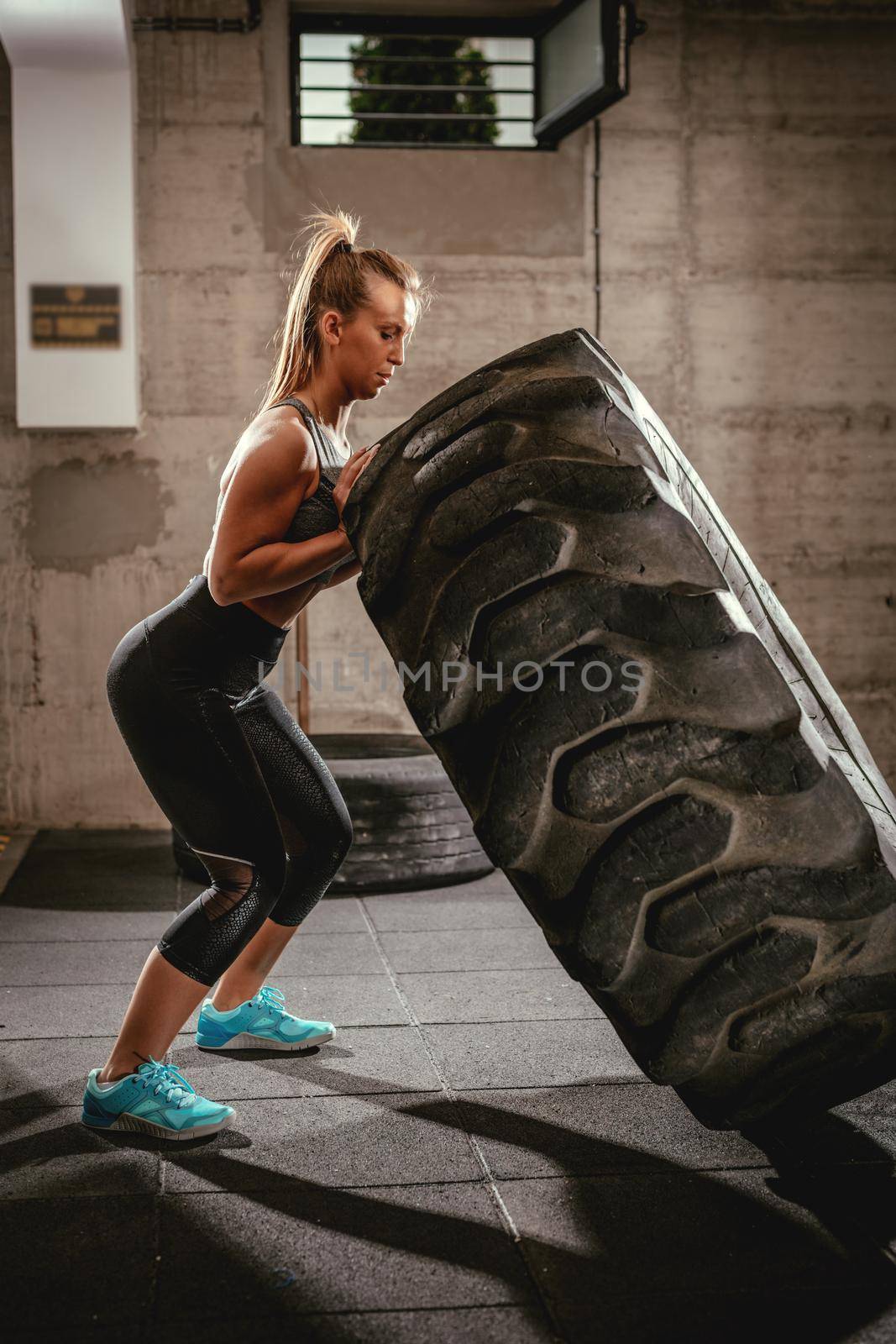 Young muscular woman flipping a tire on cross fit training at the gym.