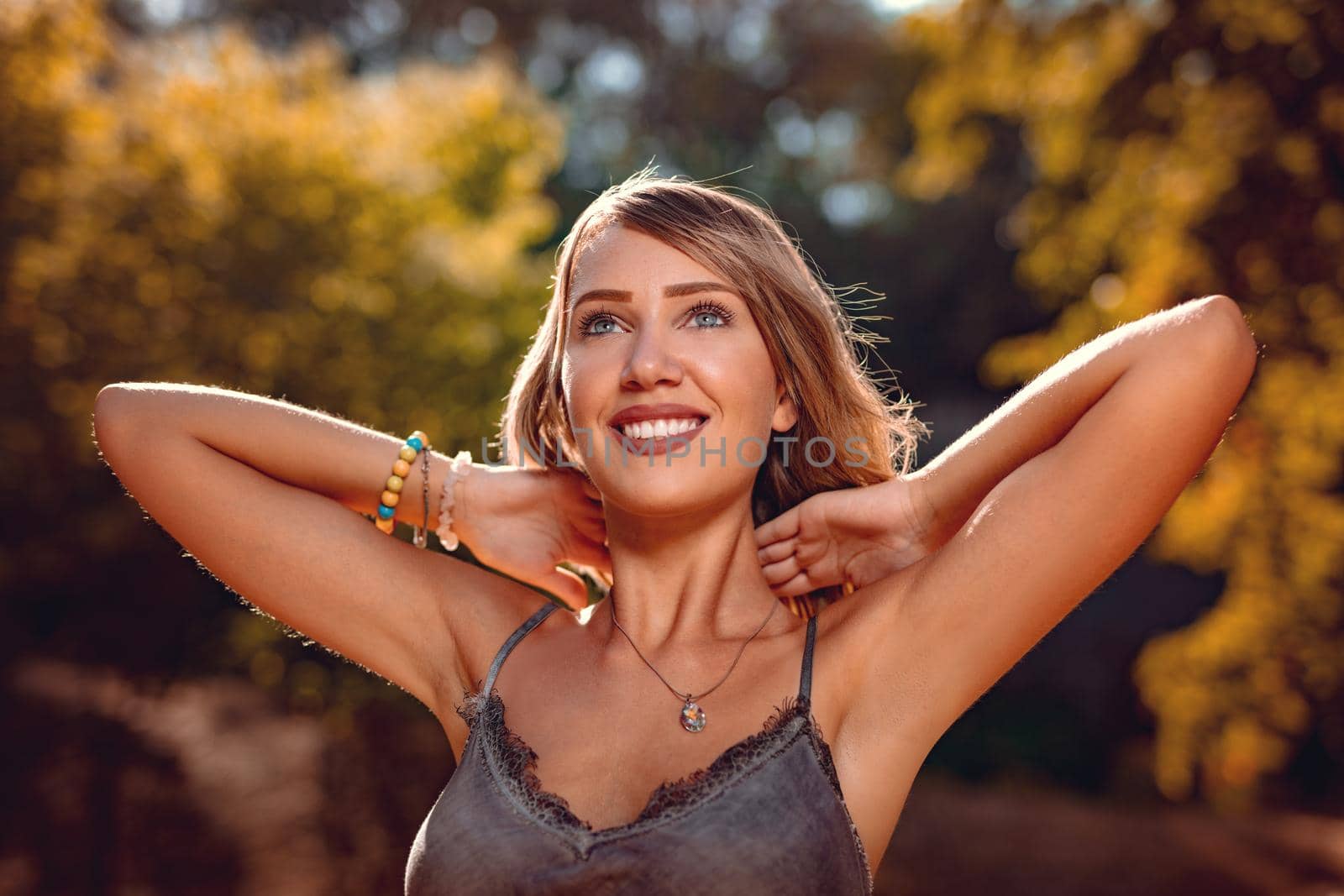 Portrait of a beautiful smiling young woman in the nature in early autumn sunny day. Looking away.