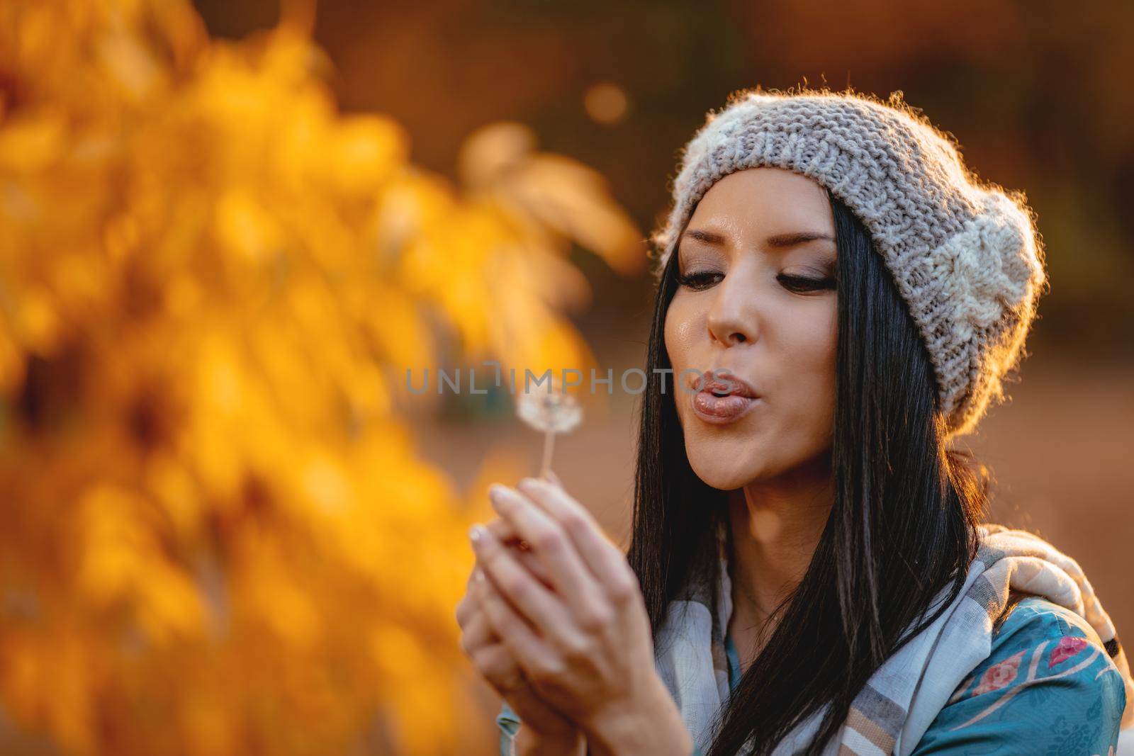 Portrait of young positive beautiful smiling young woman blowing dandelion in autumn park.
