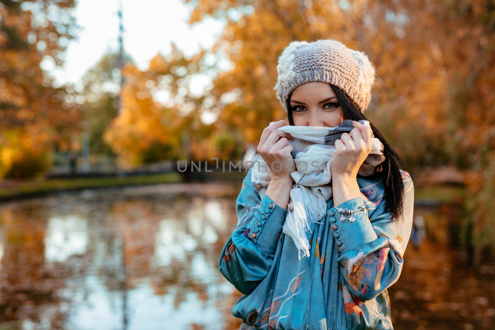 Young woman walking near the lake in a city park in a wonderful autumn day. She is tucking a shawl.