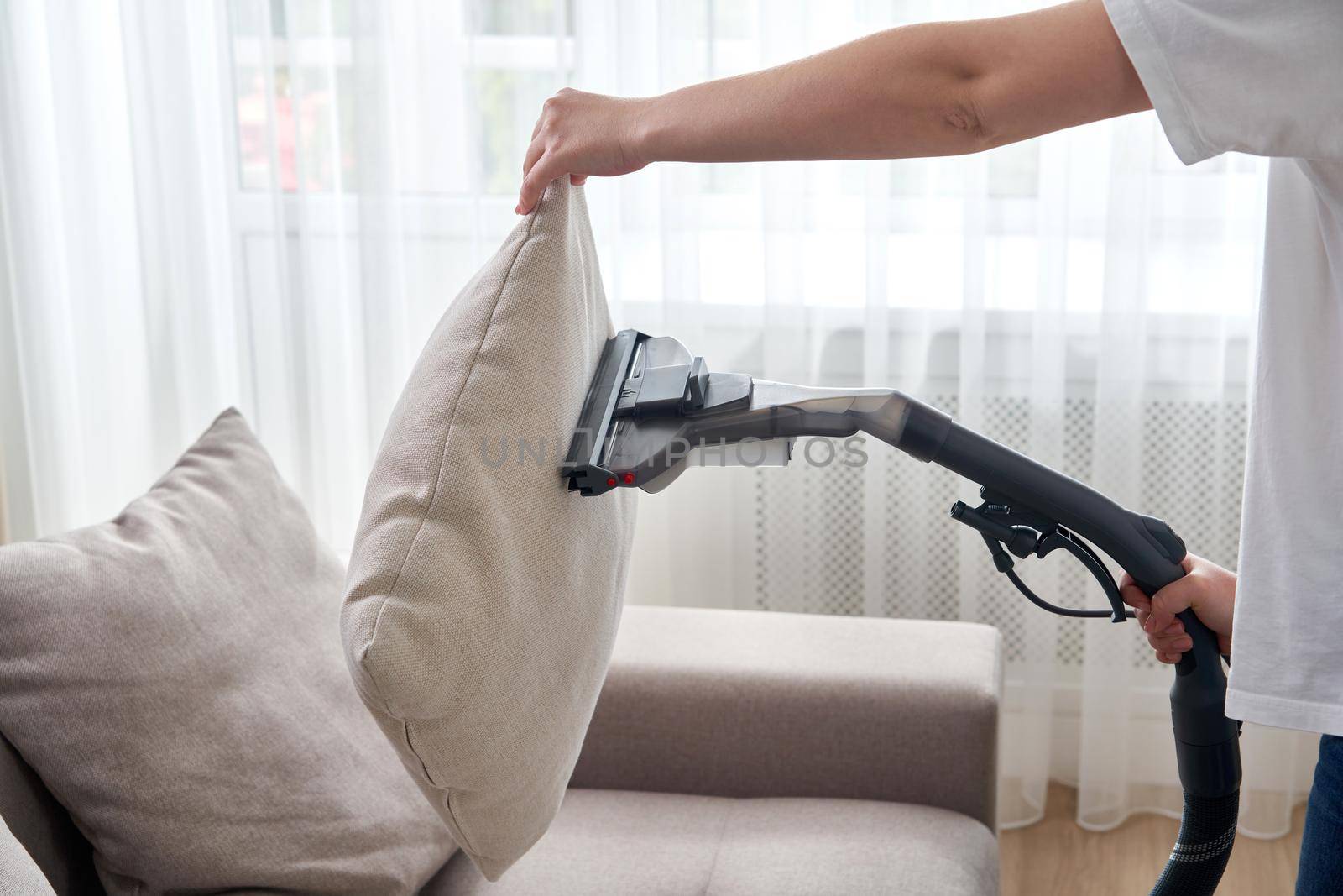 Young housewife Cleaning the Sofa with Vacuum Cleaner in living room