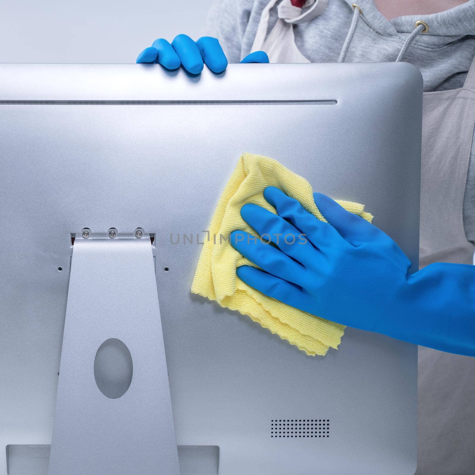 Young woman housekeeper in apron is cleaning silver computer surface with blue gloves, wet yellow rag, close up, copy space, blank design concept.