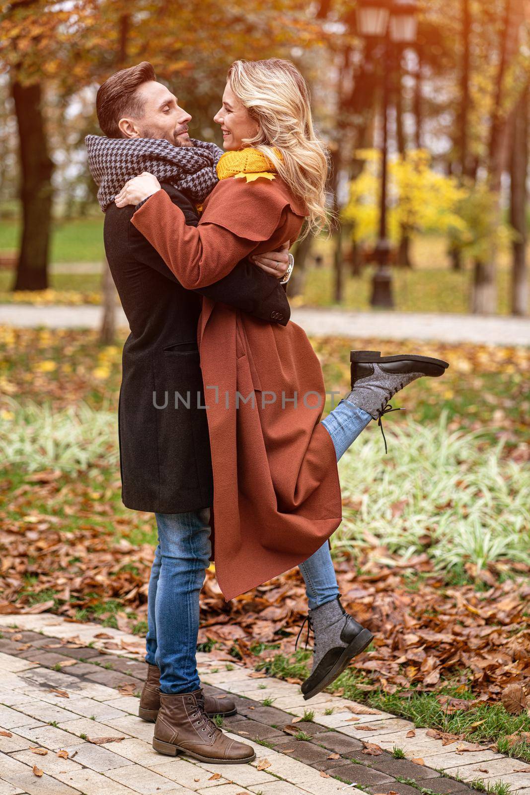 Husband lifting a wife hugged laughing in the autumn park with a cute hug. Outdoor shot of a young couple in love having great time having a hug in a autumn park. Tinted image by LipikStockMedia