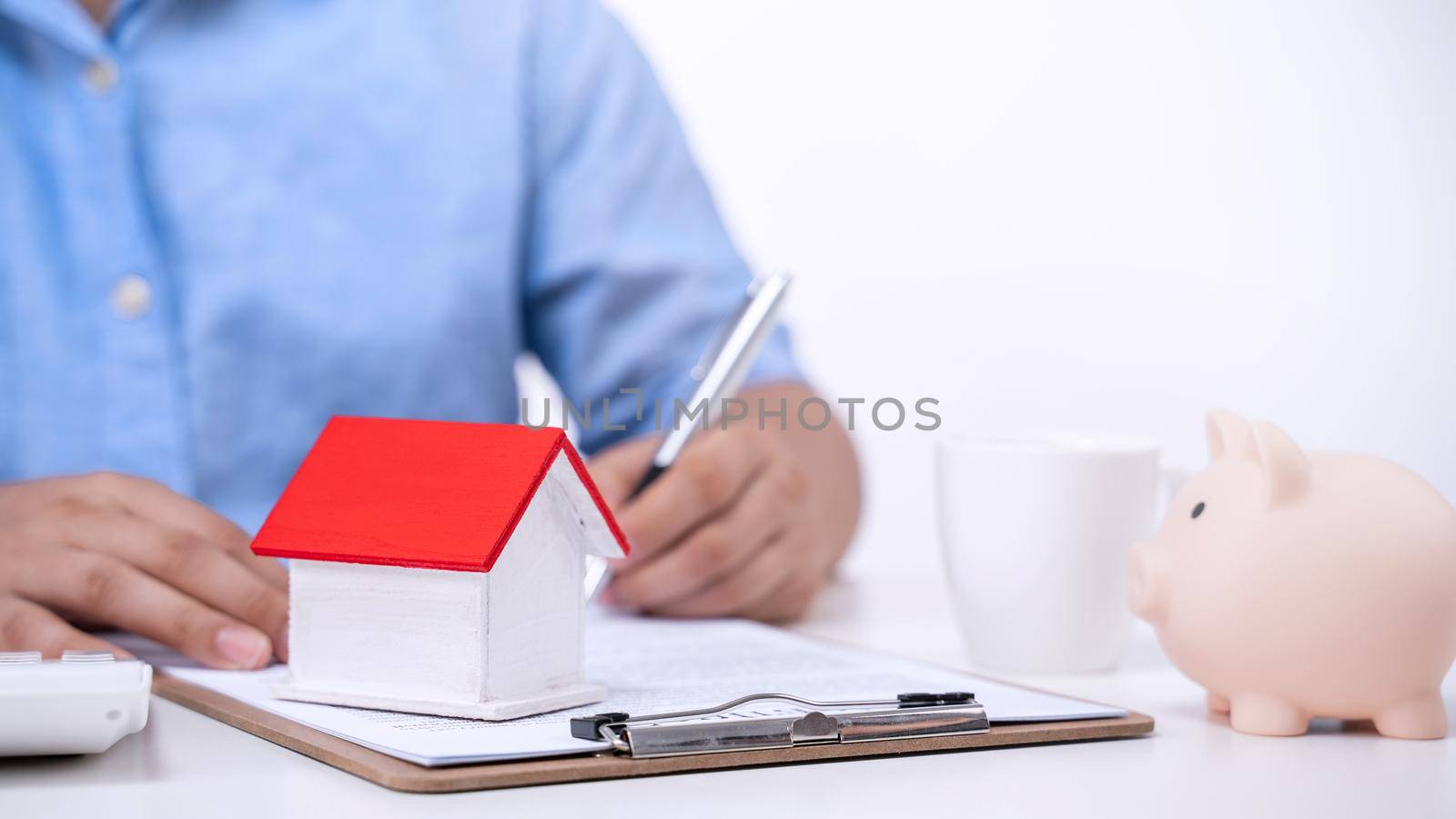 Business concept - Young Asian man in blue shirt calculates, signs agreement contract to buy a house loan payment, paying insurance, tax, close up. by ROMIXIMAGE