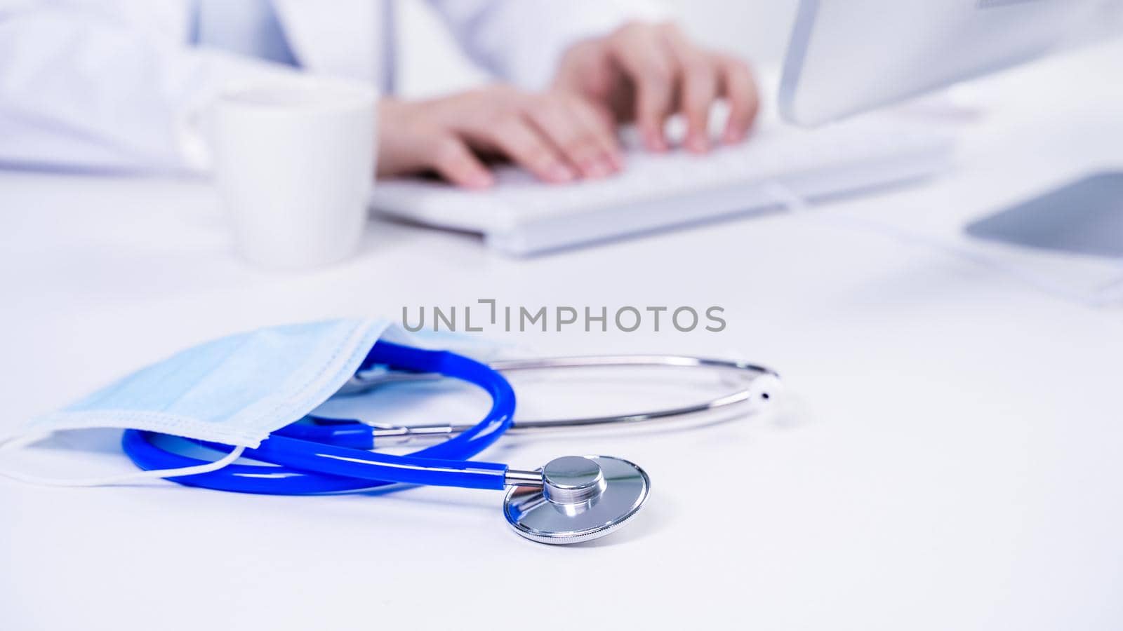 Business concept - Young female doctor woman working at office with computer, typing electronic medical record, white table background, close up, copy space