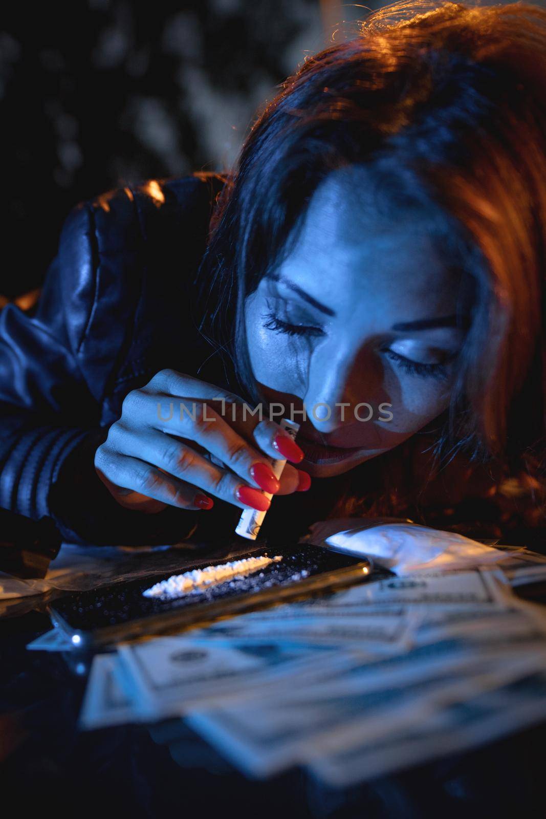 Close-up of a young drug addict woman who sniffing cocaine lines on mirror with rolled banknote in addiction and drugs abuse problem.