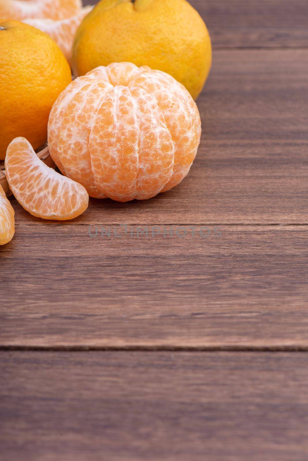Fresh, beautiful orange color tangerine on bamboo sieve over dark wooden table. Seasonal, traditional fruit of Chinese lunar new year, close up. by ROMIXIMAGE