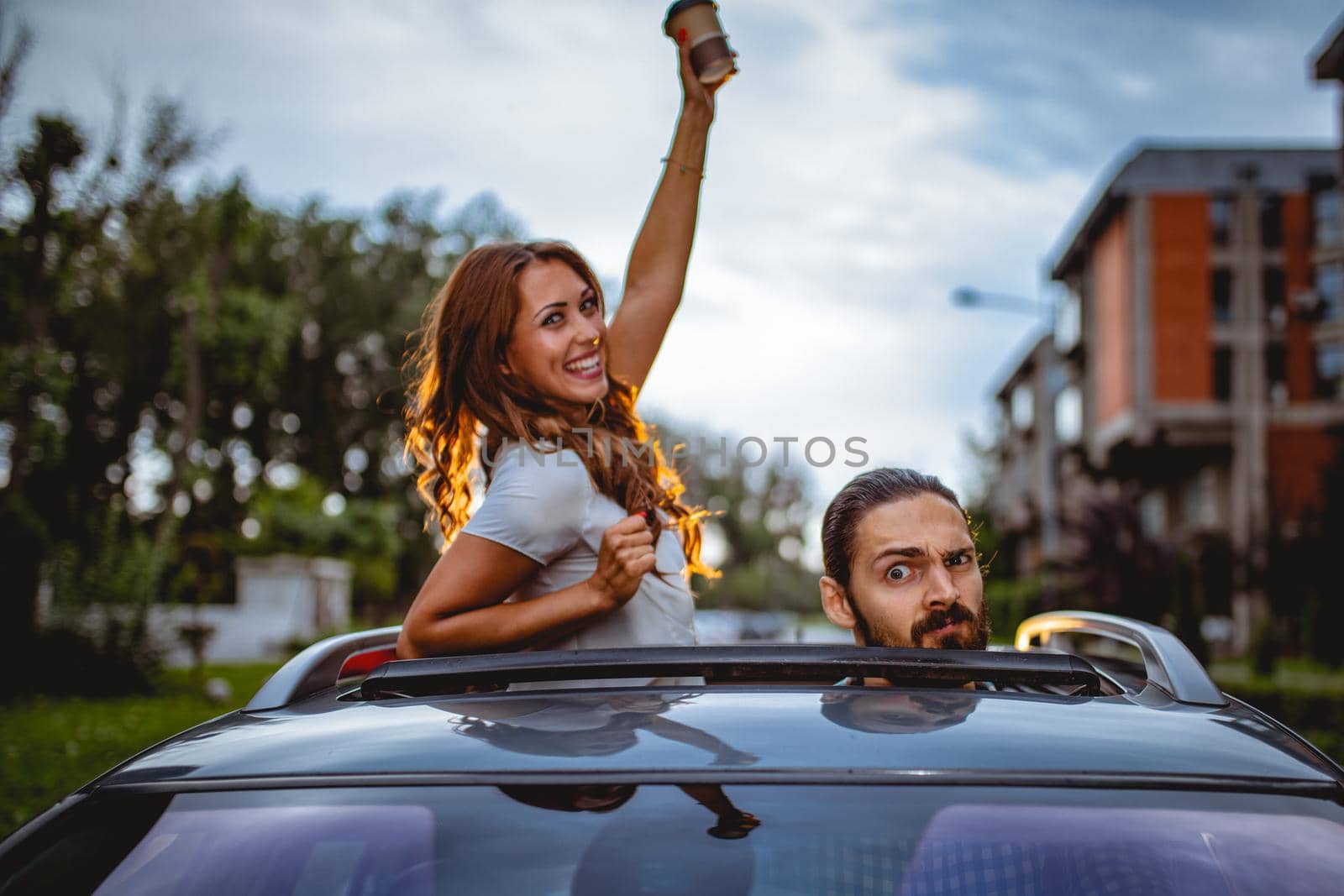 Young crazy couple having fun during driving car, peeping through the sunroof during the driving.