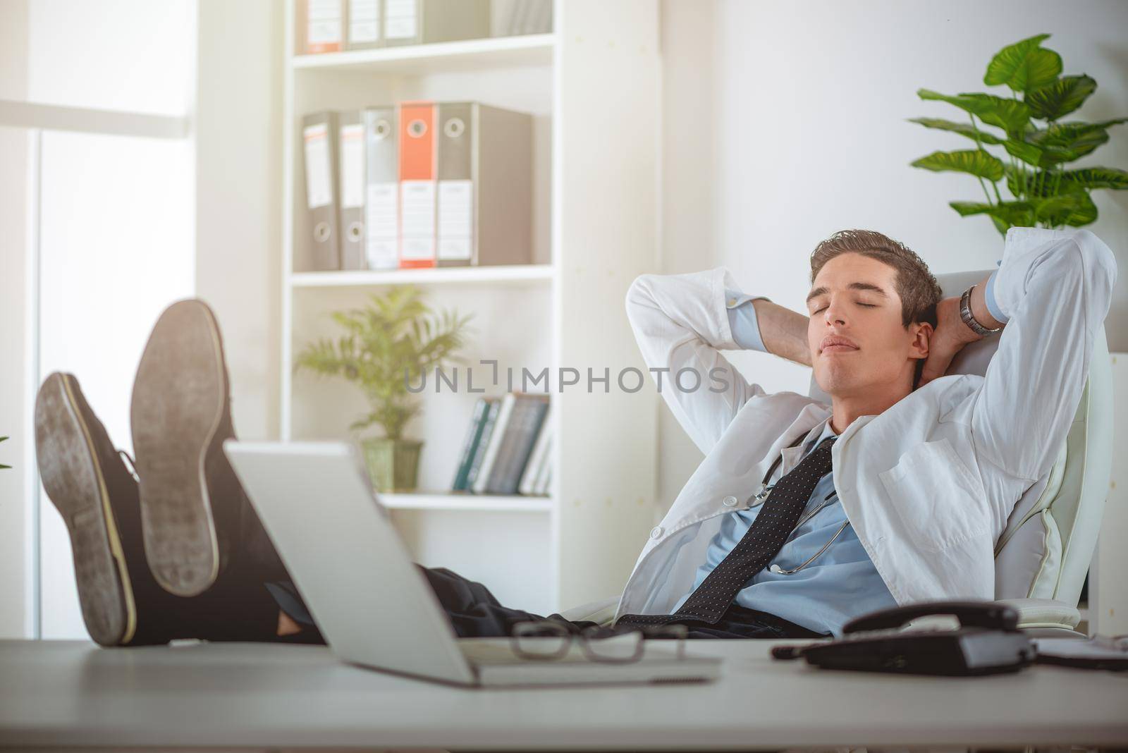 Overworked, tired young businessman sleeping at his desk in office, in front of computer.