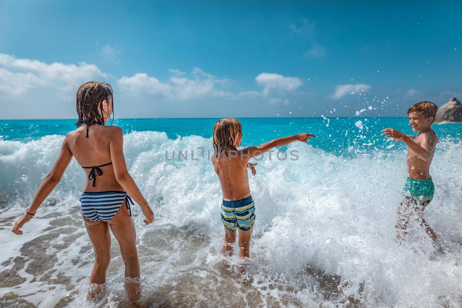 Brothers and sister playing in the shore on the beach during the hot summer vacation day.