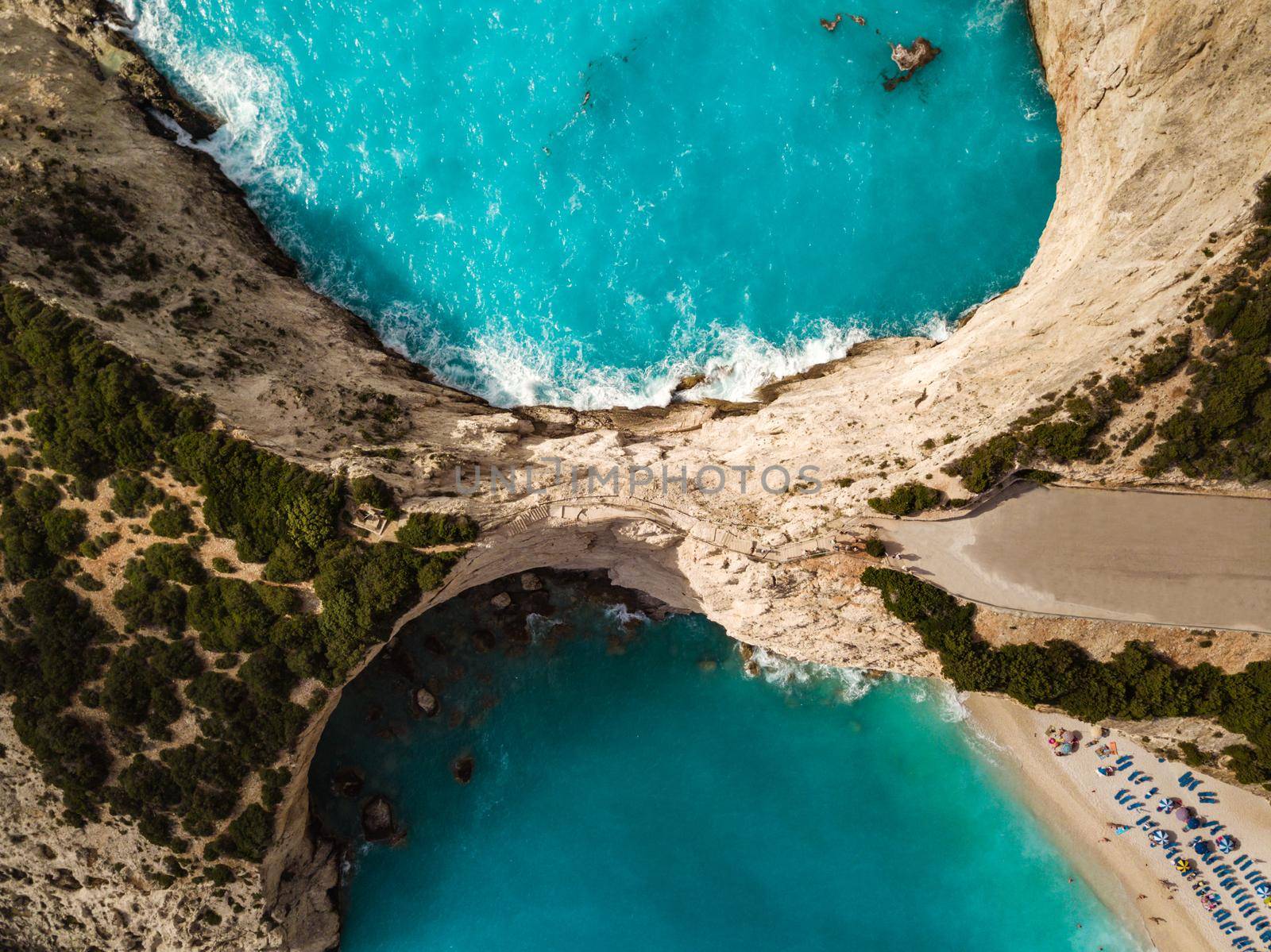 Aerial views of the turquoise sea water with wild seashore and waves reaching sandy beach and steeply rocks on a sunny day. 