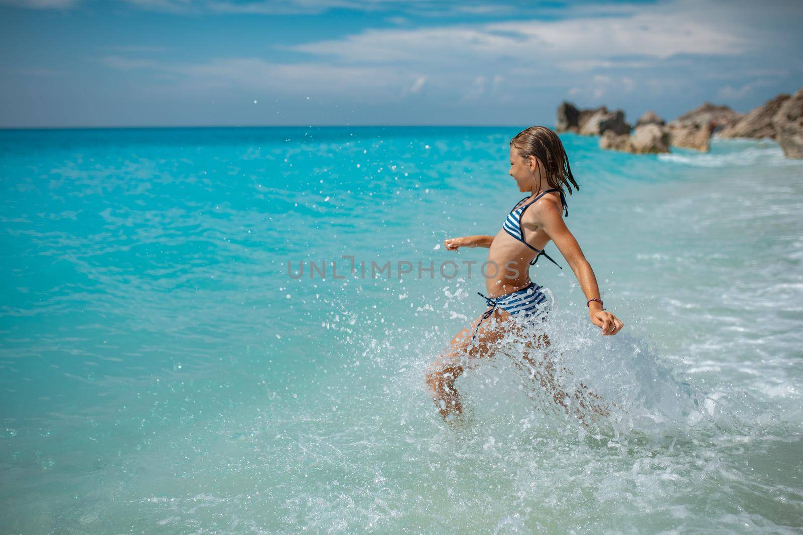 A little girl having fun in the waves of the sea and the drops of water are splashing all over her.
