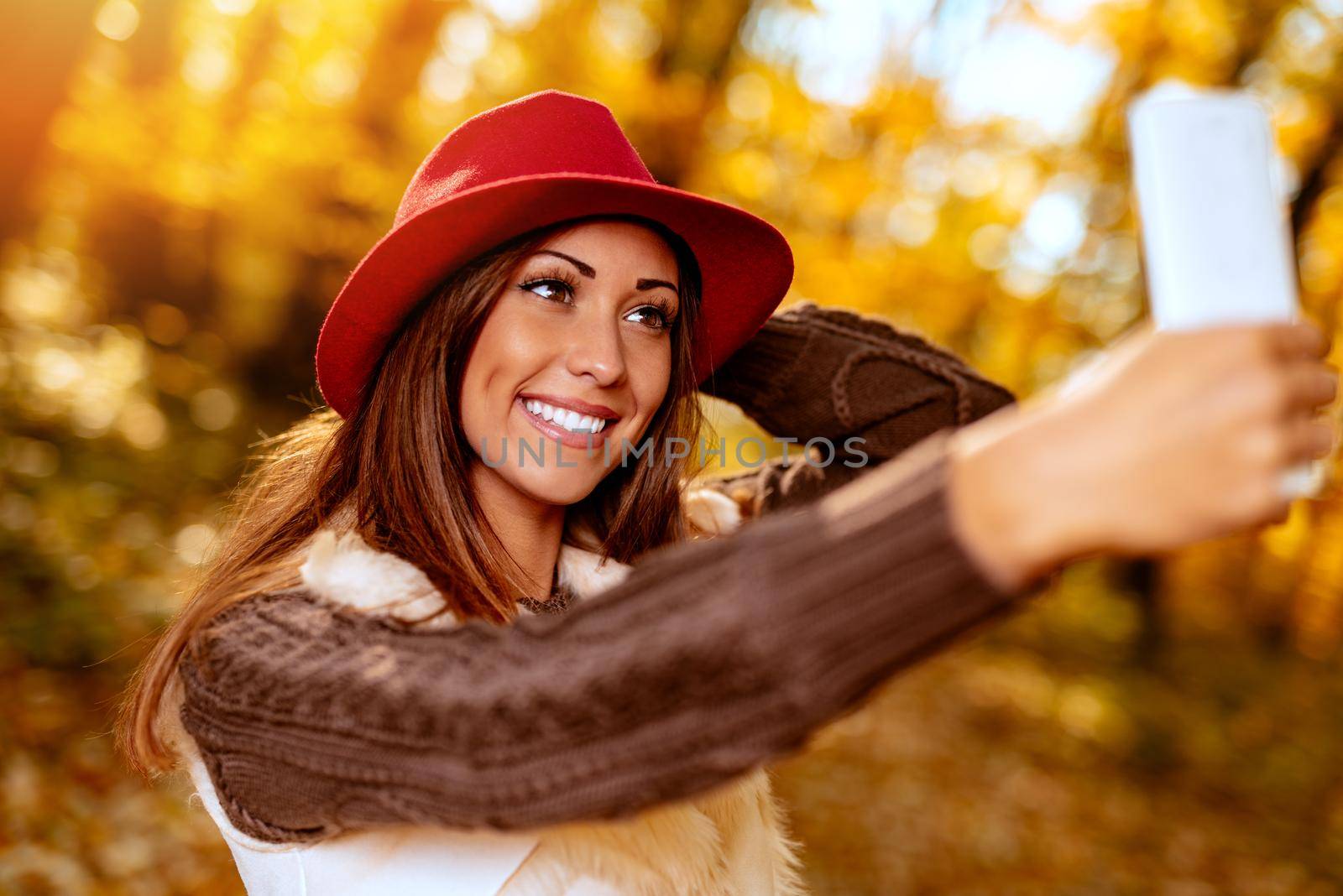 Portrait of a beautiful smiling woman taking selfie in forest in autumn.